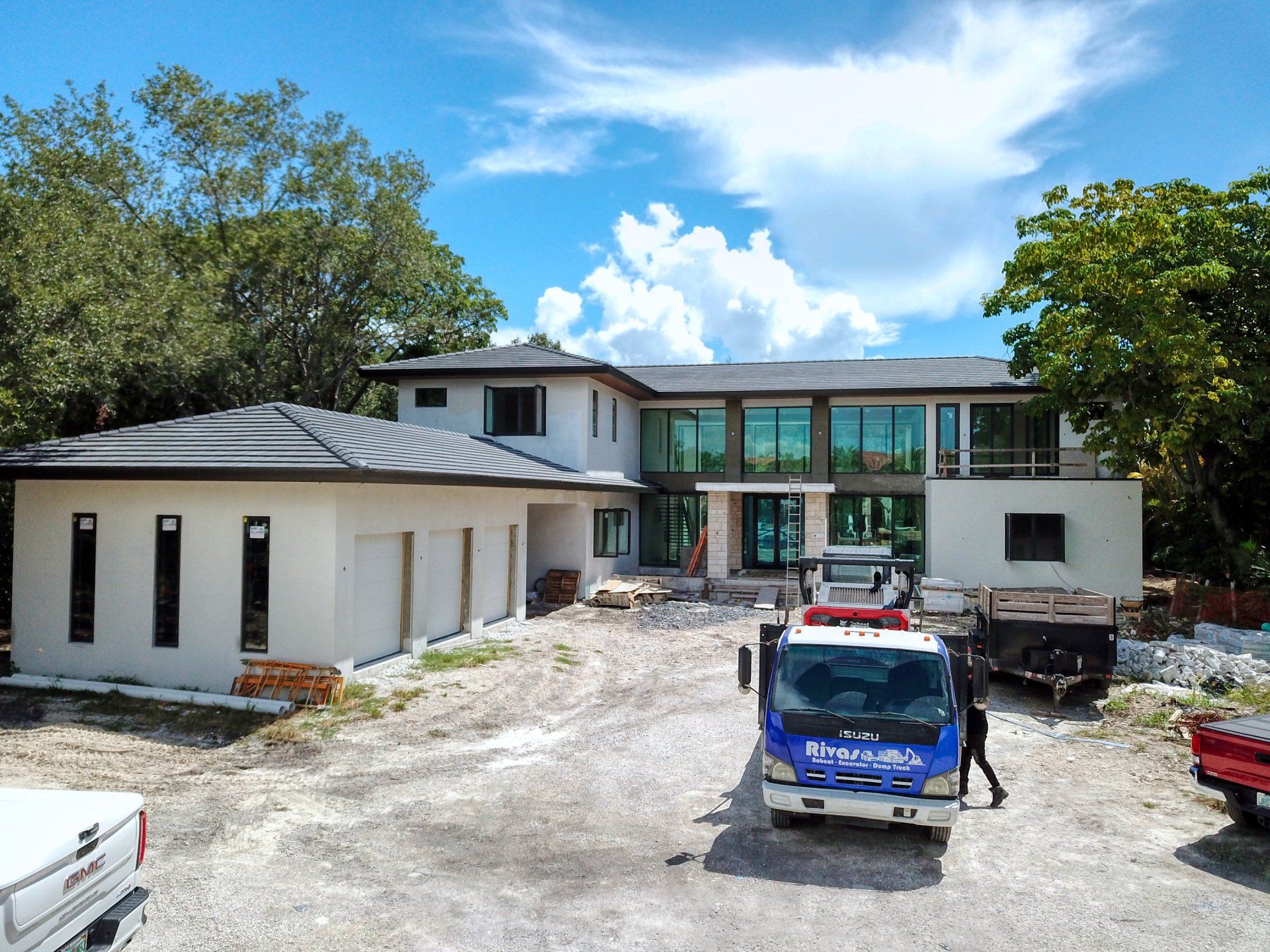 A partially constructed modern house with a truck parked in the gravel driveway under a partly cloudy sky.