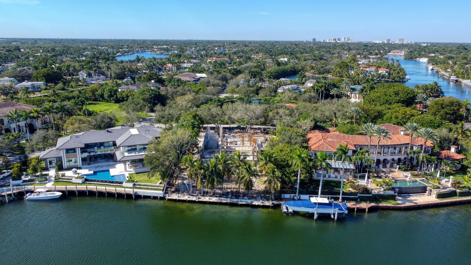 Aerial view of waterfront houses with docks, trees, and blue water under a clear sky.