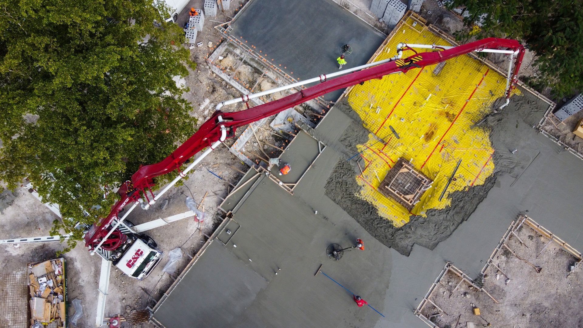 Construction site: Concrete being poured by a red boom truck onto a yellow-walled foundation.