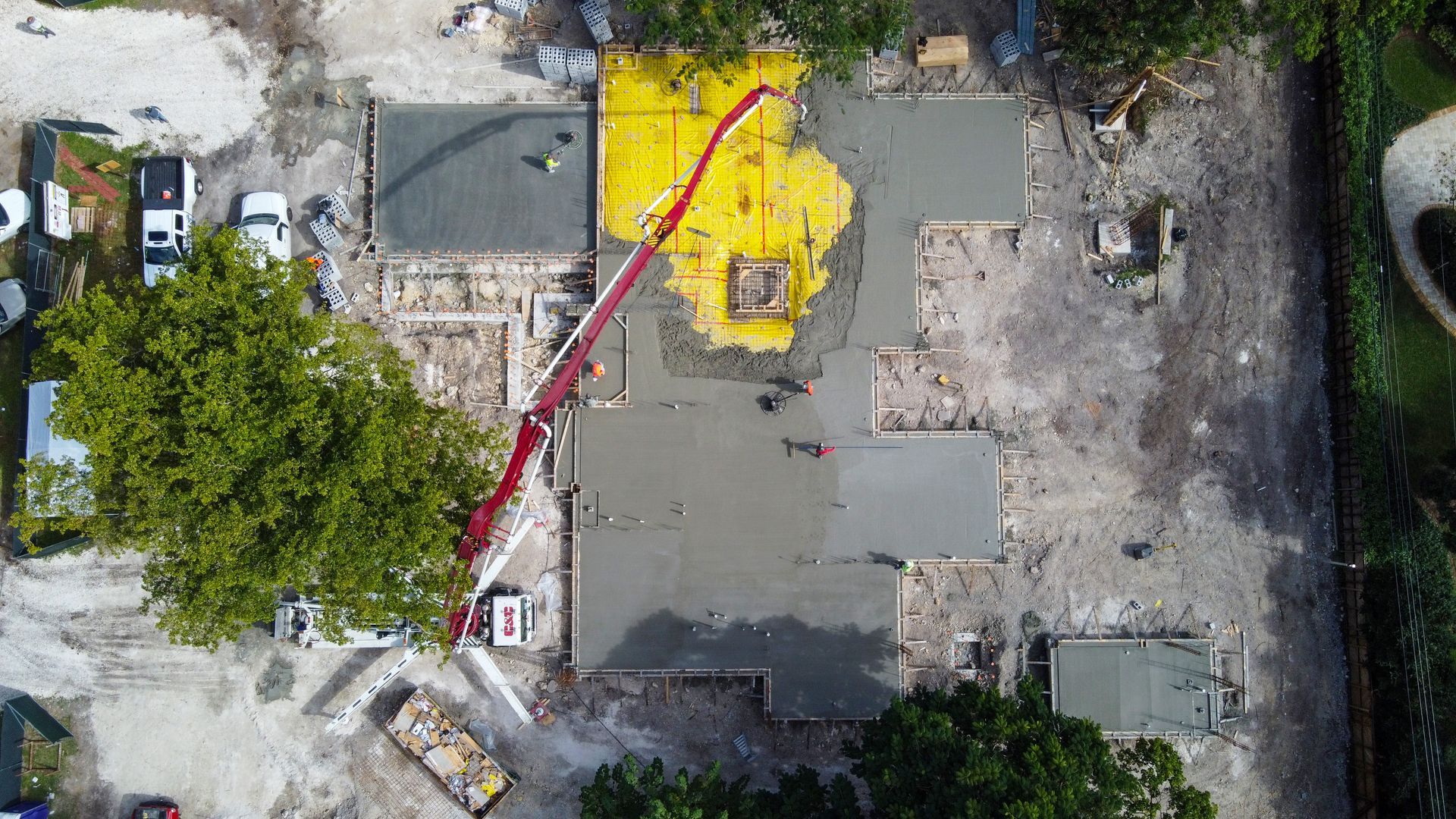 Aerial view of a construction site: concrete being poured with a boom pump into the foundation of a building.