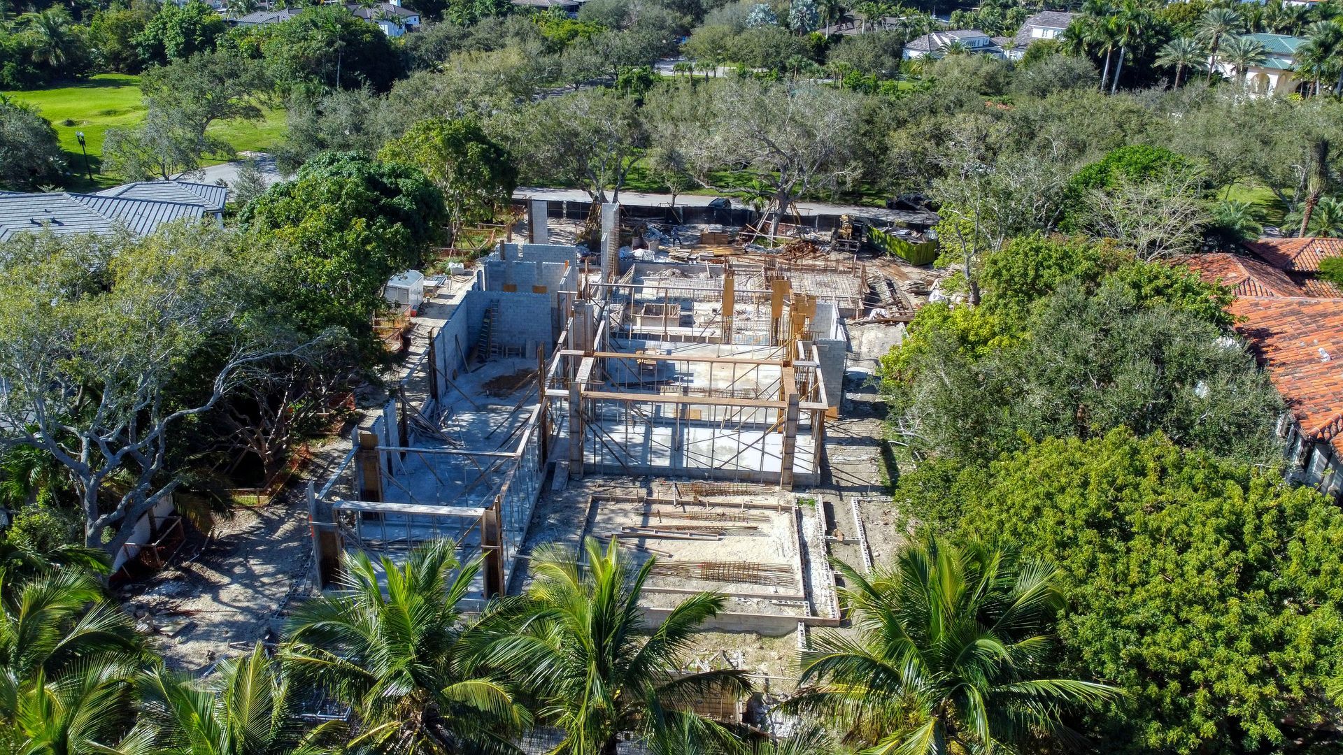 Aerial view of construction site surrounded by trees; concrete foundations and wooden framework visible.