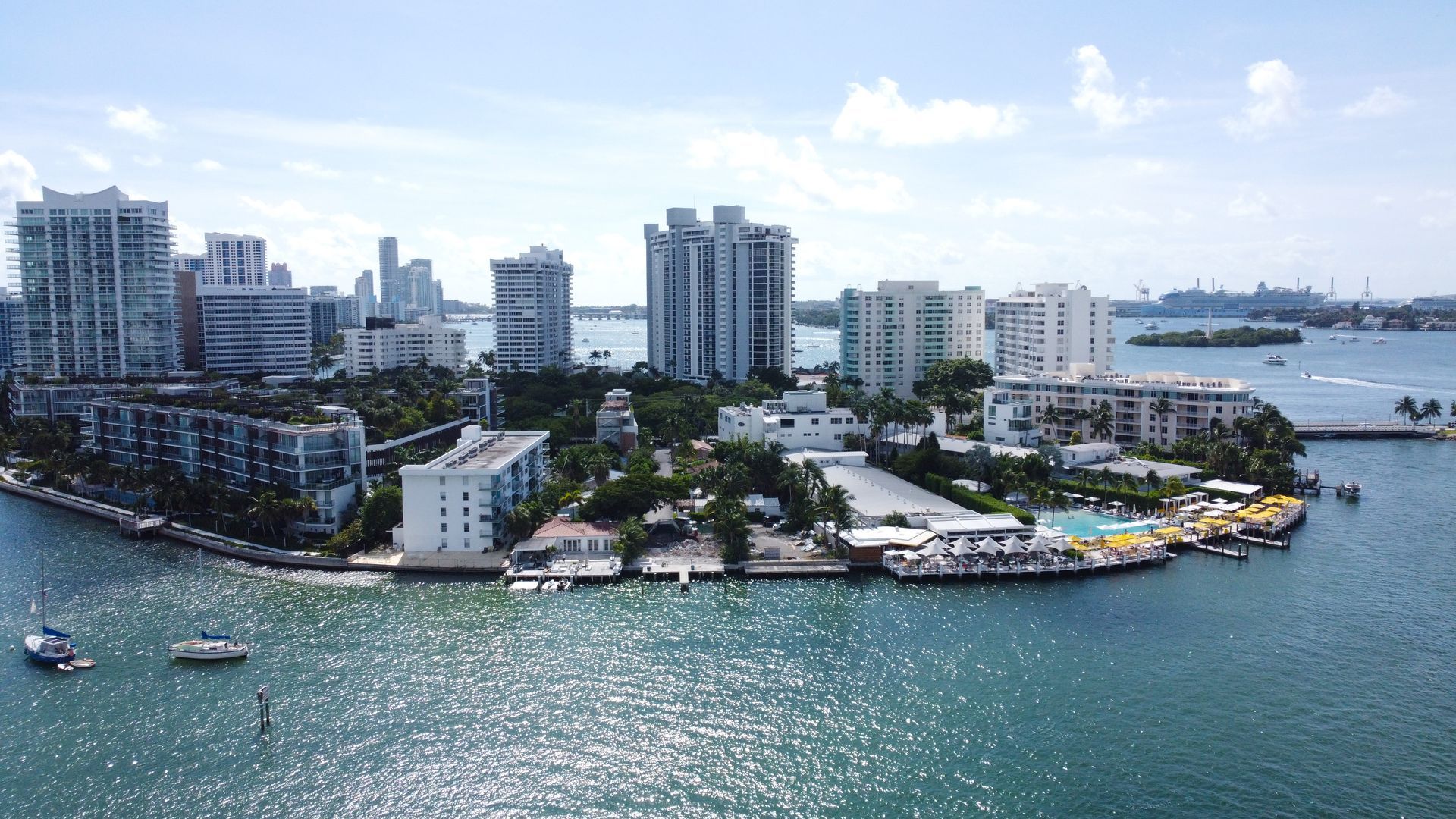 City buildings on a waterfront, sunny day. White and blue buildings surrounded by water, with boats visible.