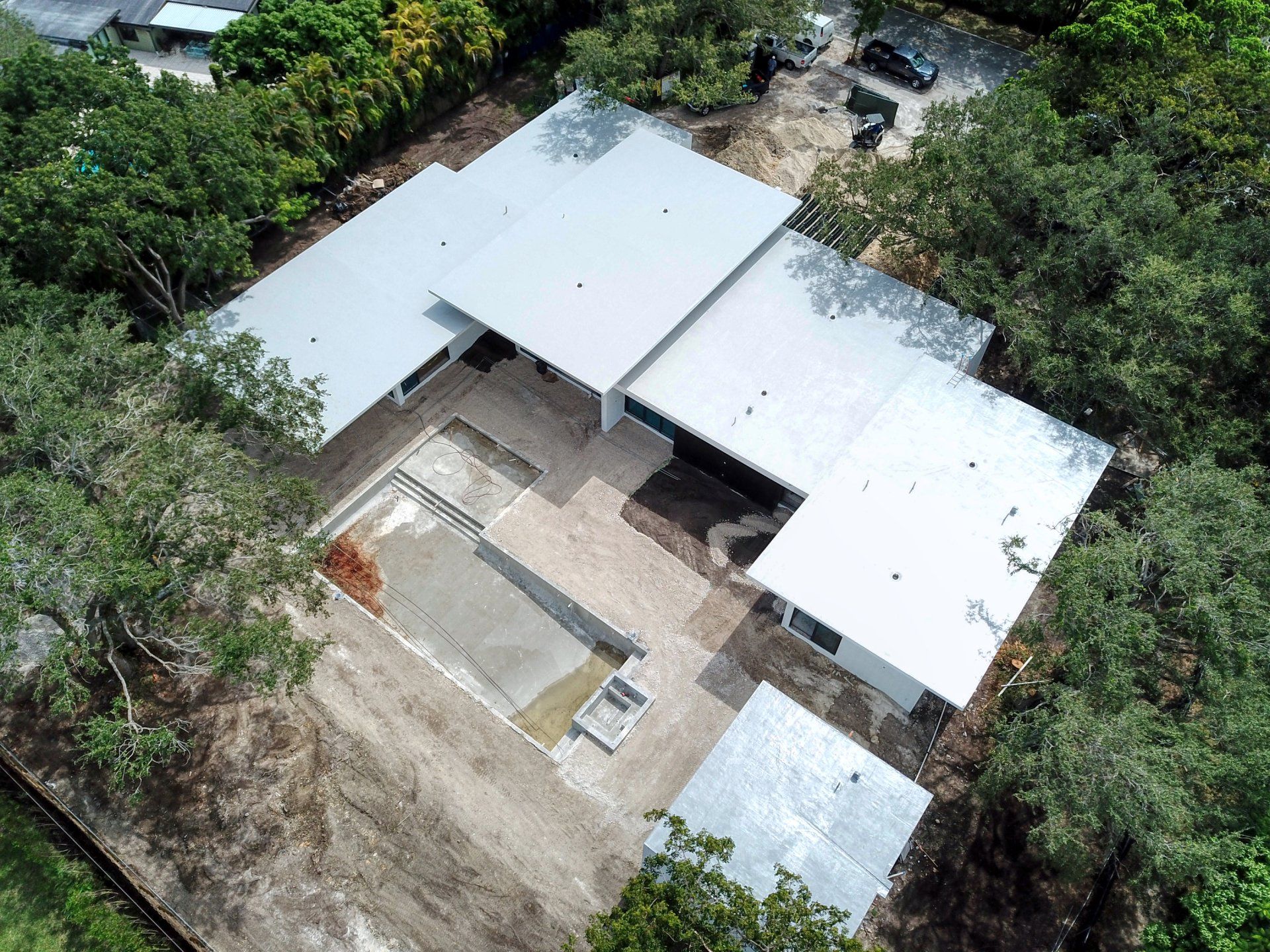 Aerial view of a modern house with a pool under construction, surrounded by trees.