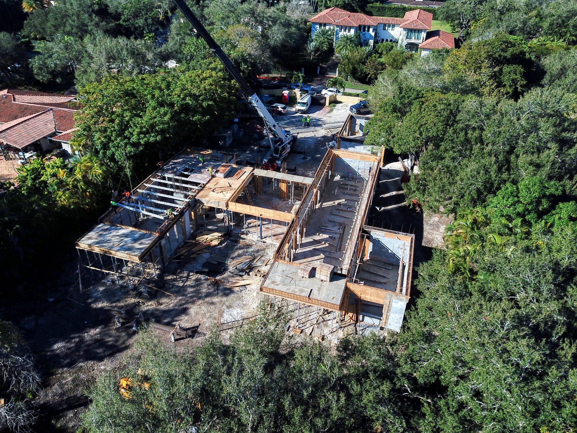 Aerial view of a building under construction, wooden frame, crane, surrounded by trees.