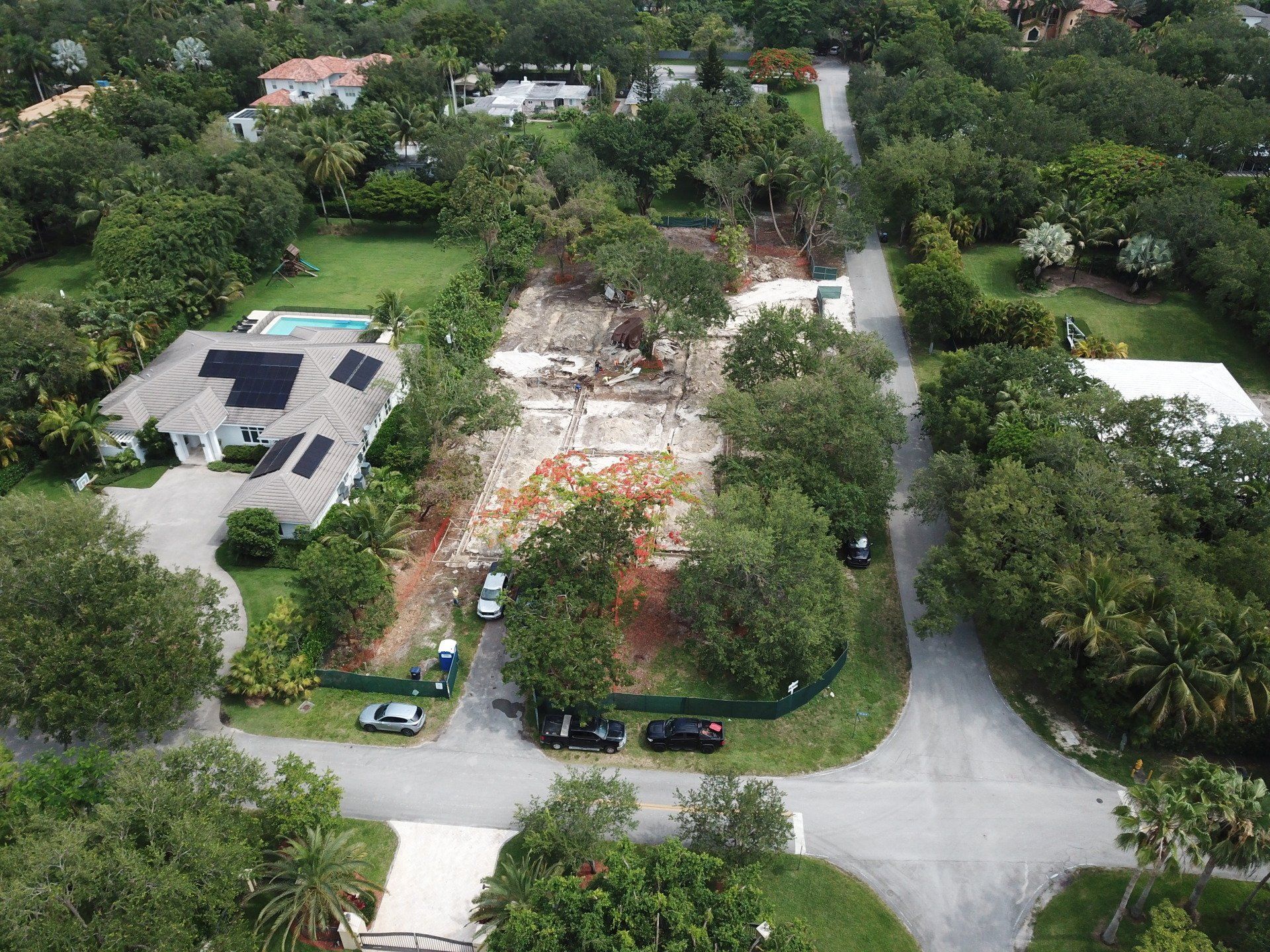 Aerial view of construction site surrounded by trees and residential houses.