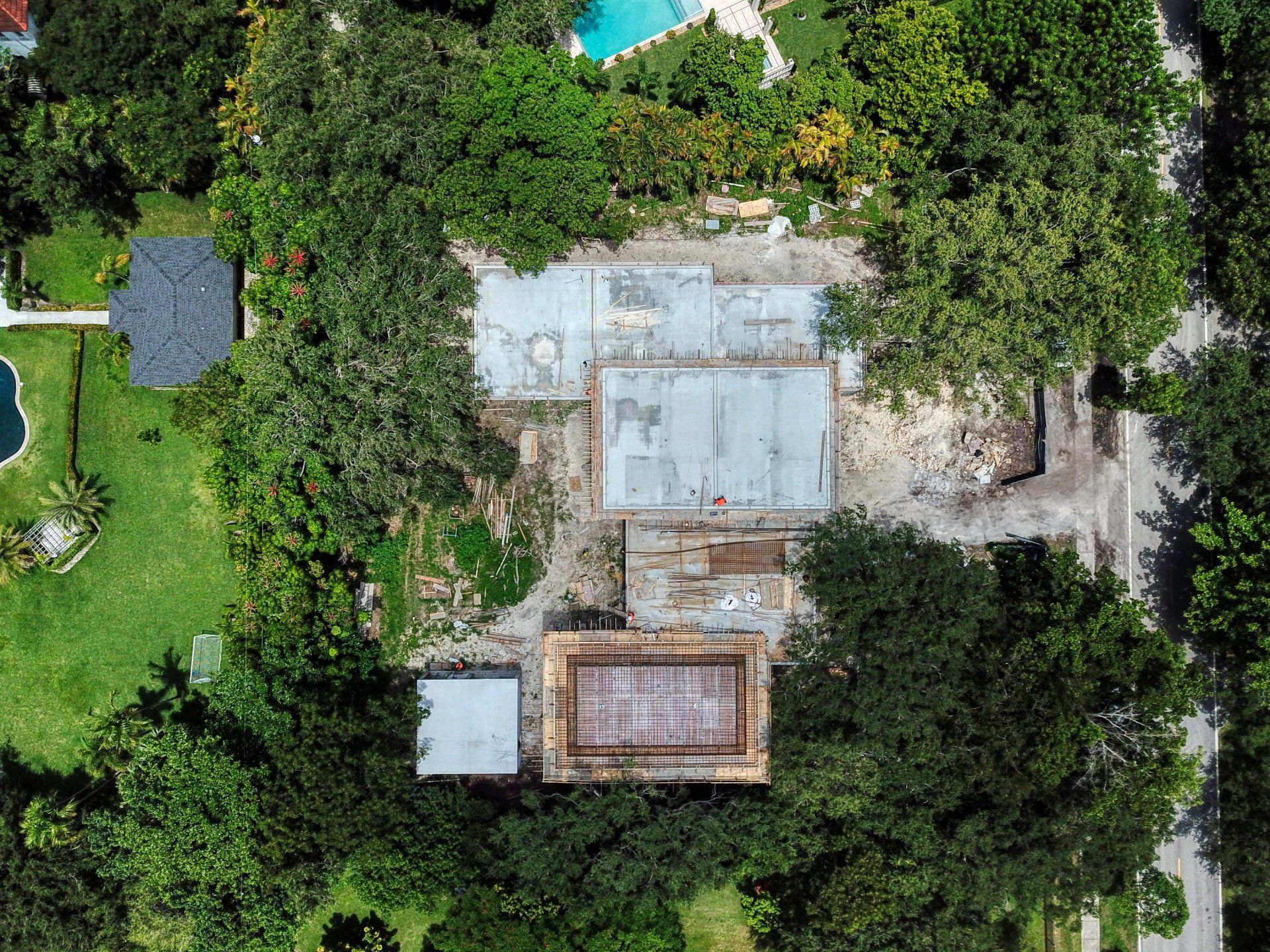 Aerial view of a home being renovated, surrounded by trees and a pool. Gray roofing, green grass.