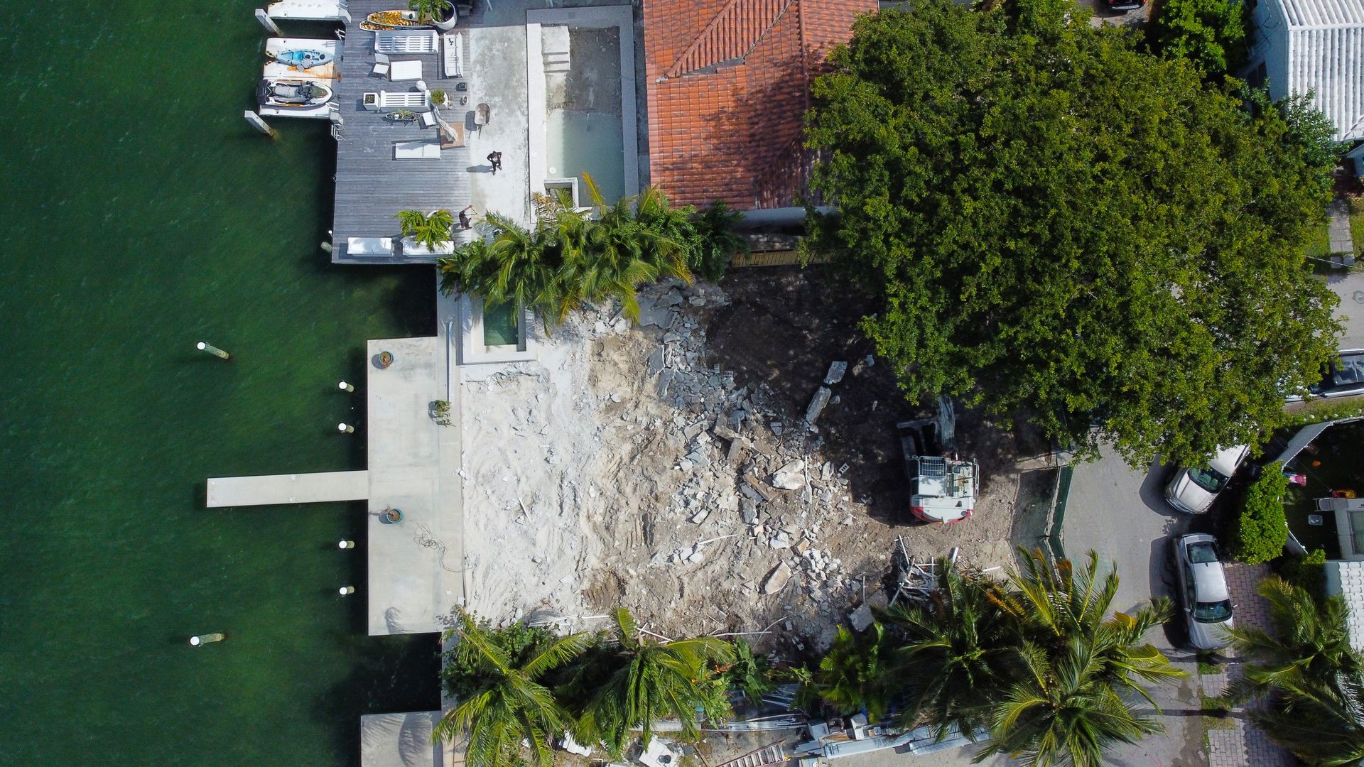 Overhead view: Construction site on waterfront property with debris, trees, and water.