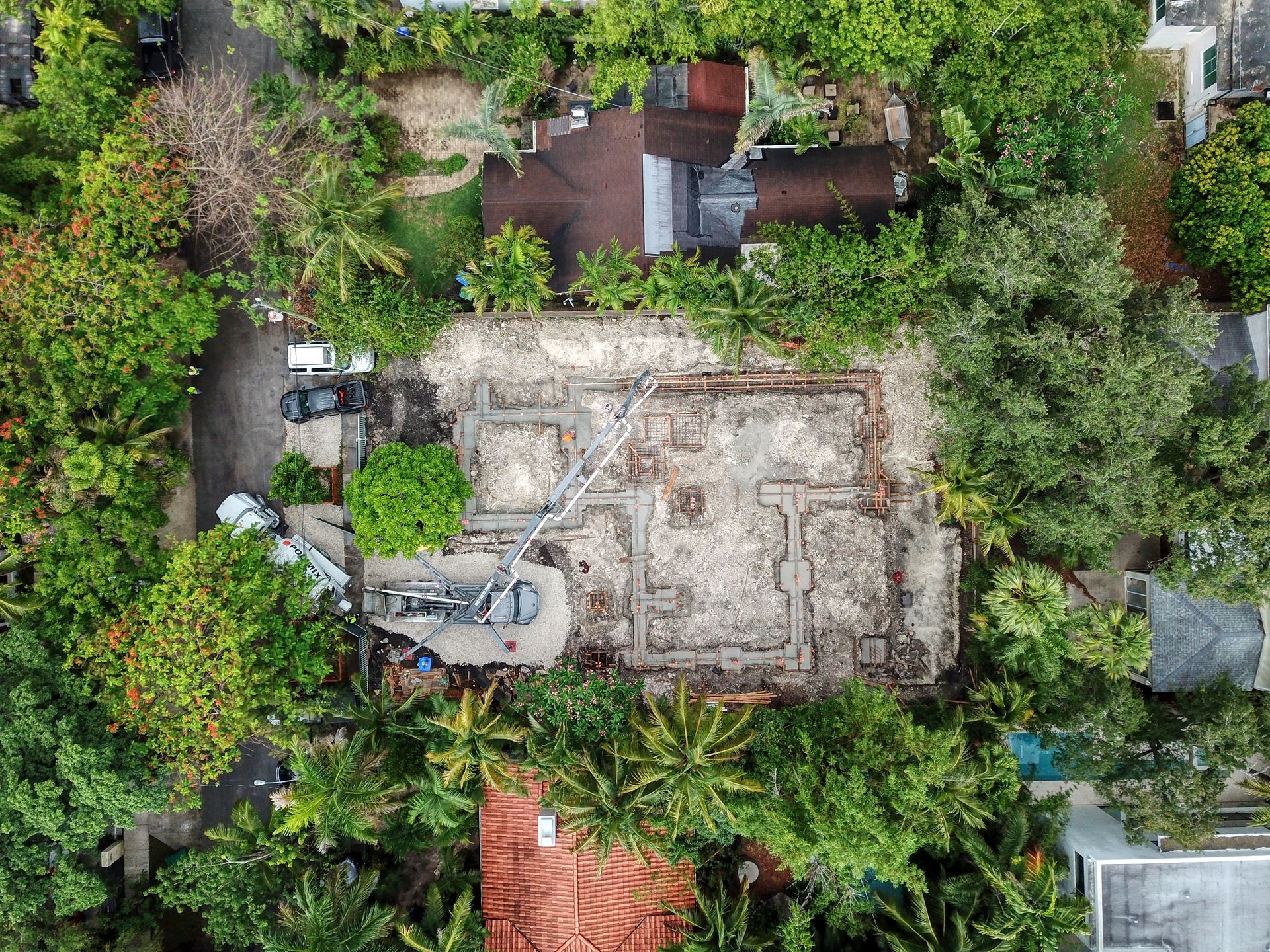 Overhead view of a construction site with debris surrounded by green trees and buildings.