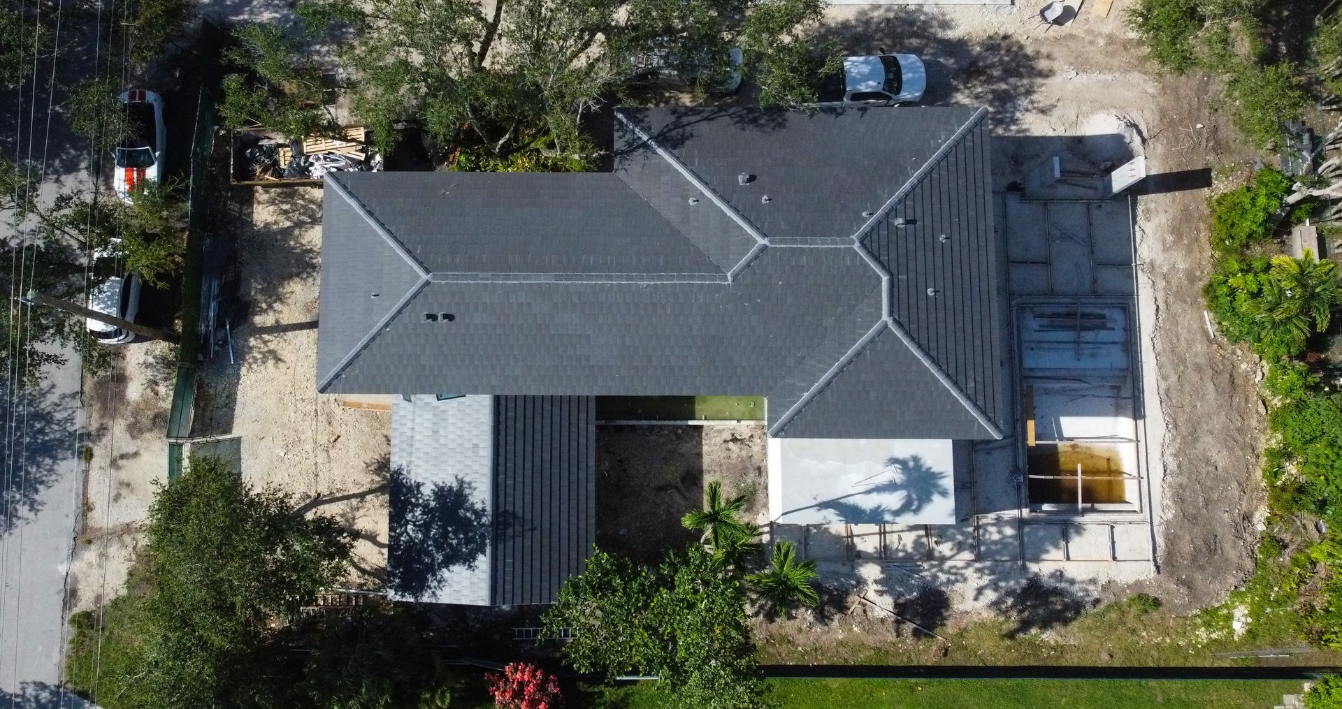 Aerial view of a house with a dark gray roof surrounded by dirt and trees.