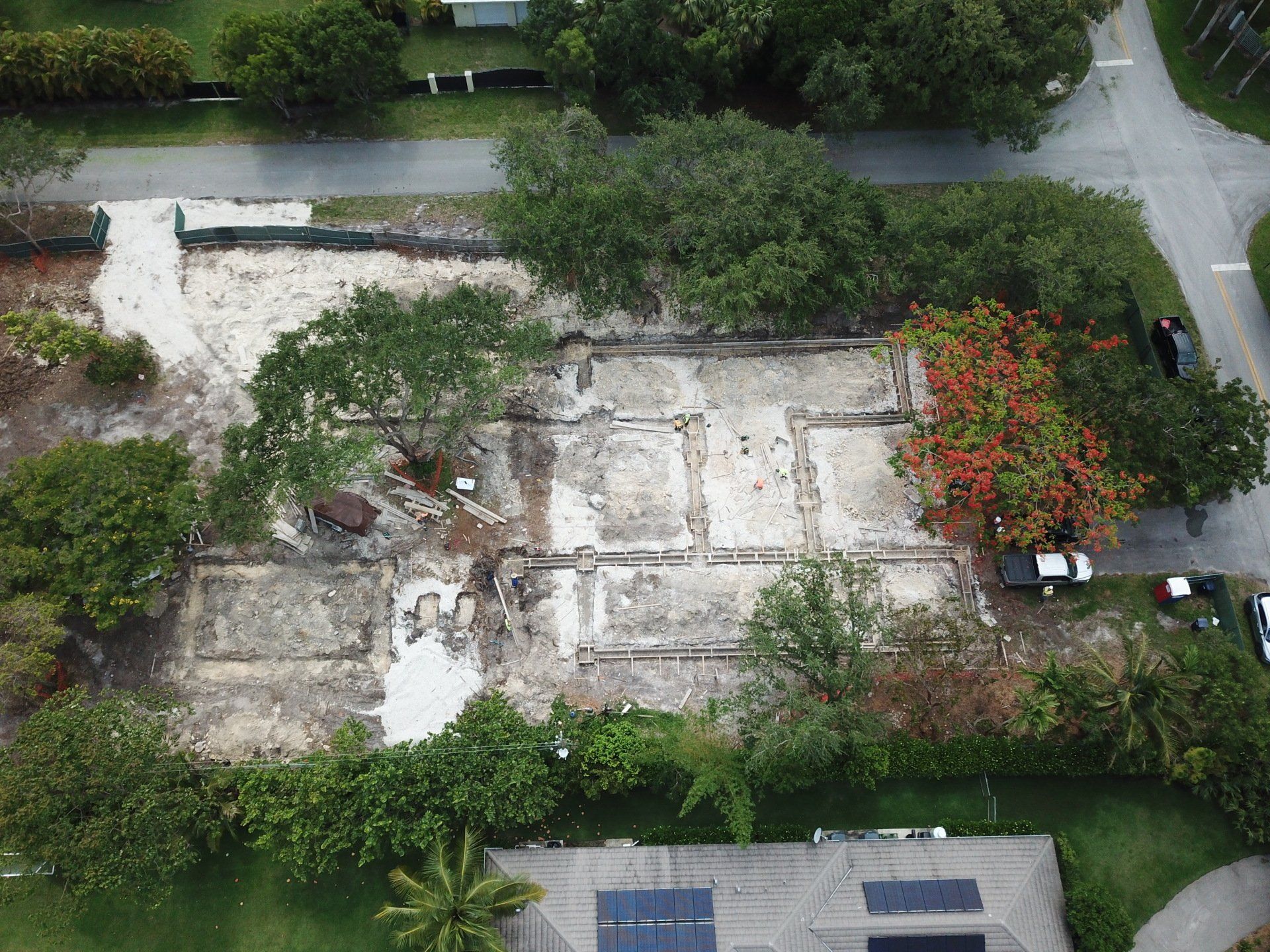 Aerial view of a cleared construction site with remnants of a foundation and surrounding trees and vegetation.
