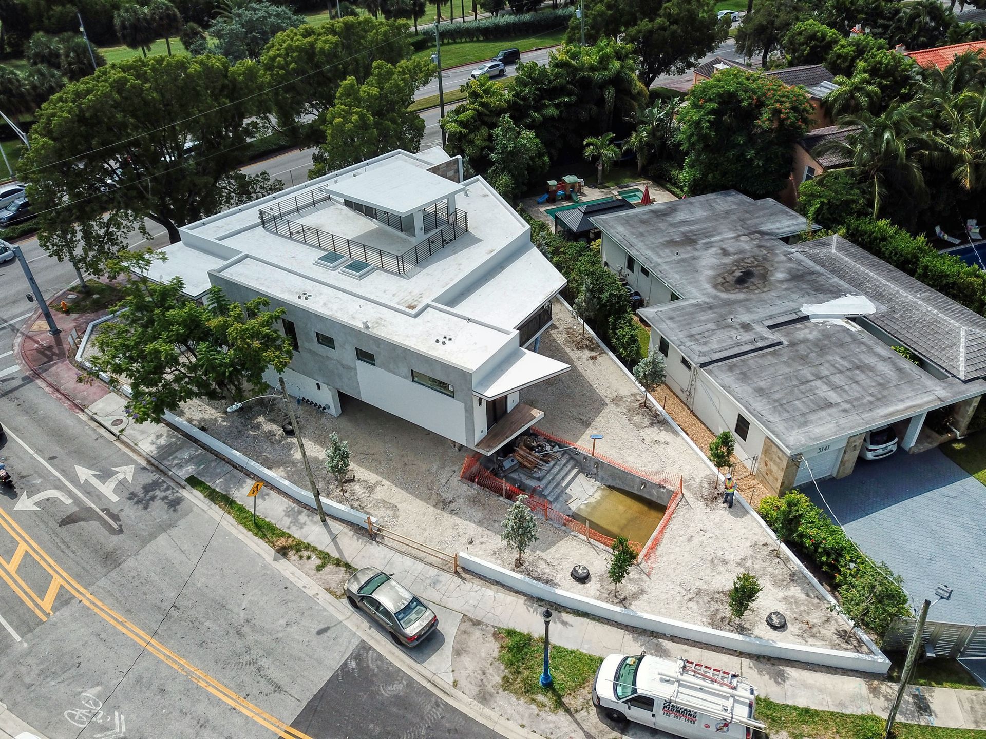 Aerial view of a modern, multi-level building with a triangular lot next to a smaller house and a street.