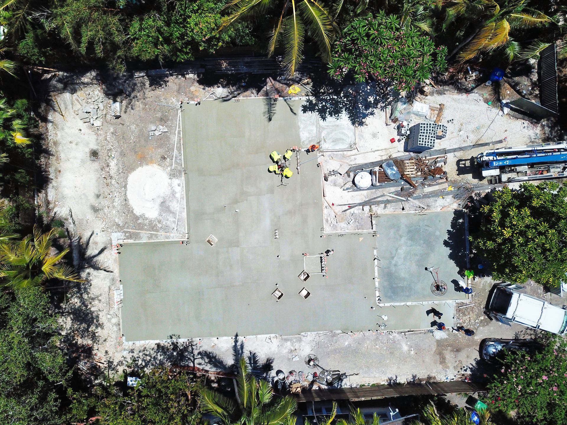 Aerial view of construction site with fresh concrete, workers, and surrounding trees.