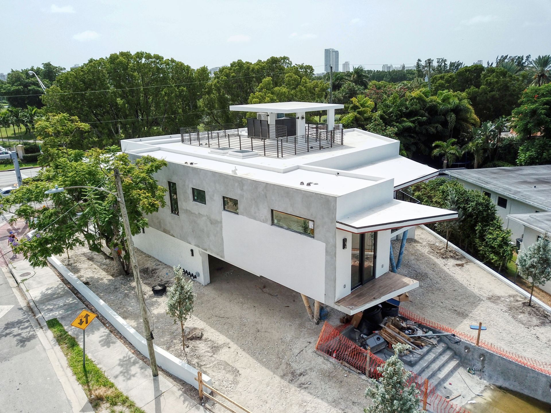Modern two-story house with a flat roof under construction. Gray and white exterior with a small wooden deck.