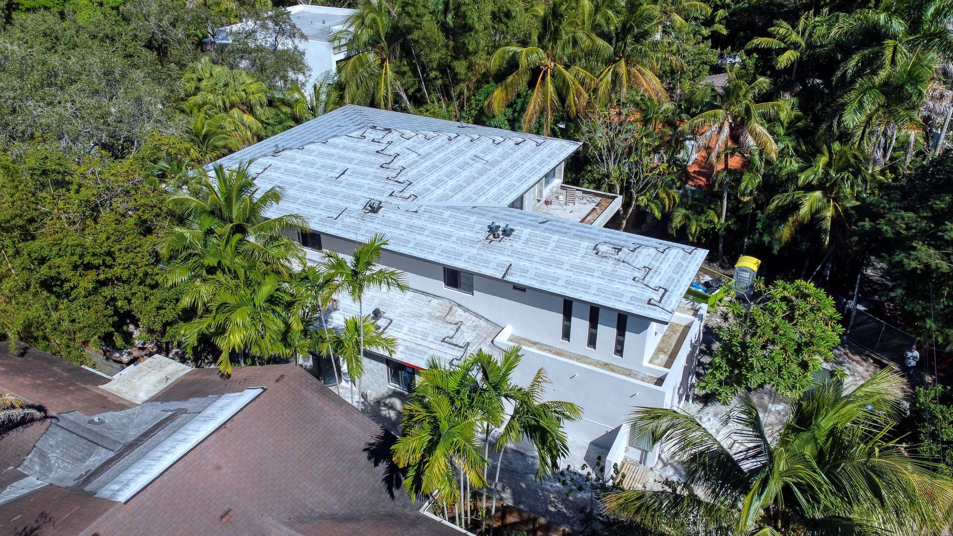 Aerial view of a gray roof house surrounded by dense green trees.
