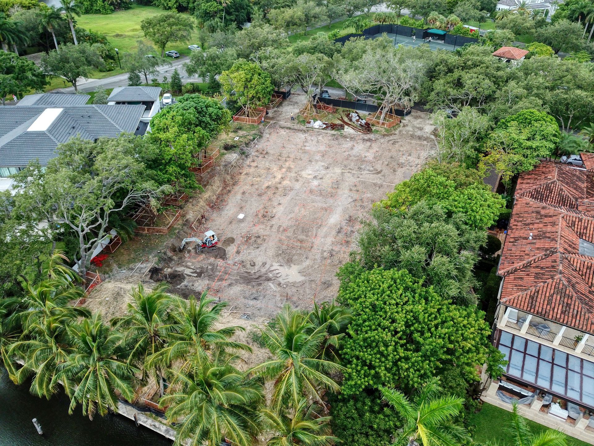Aerial view of a cleared lot surrounded by trees, with some construction debris and buildings nearby.