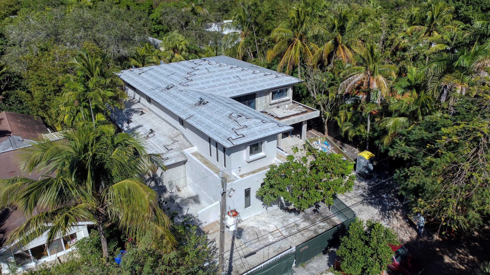 Aerial view of an unfinished, two-story gray house surrounded by lush green trees.