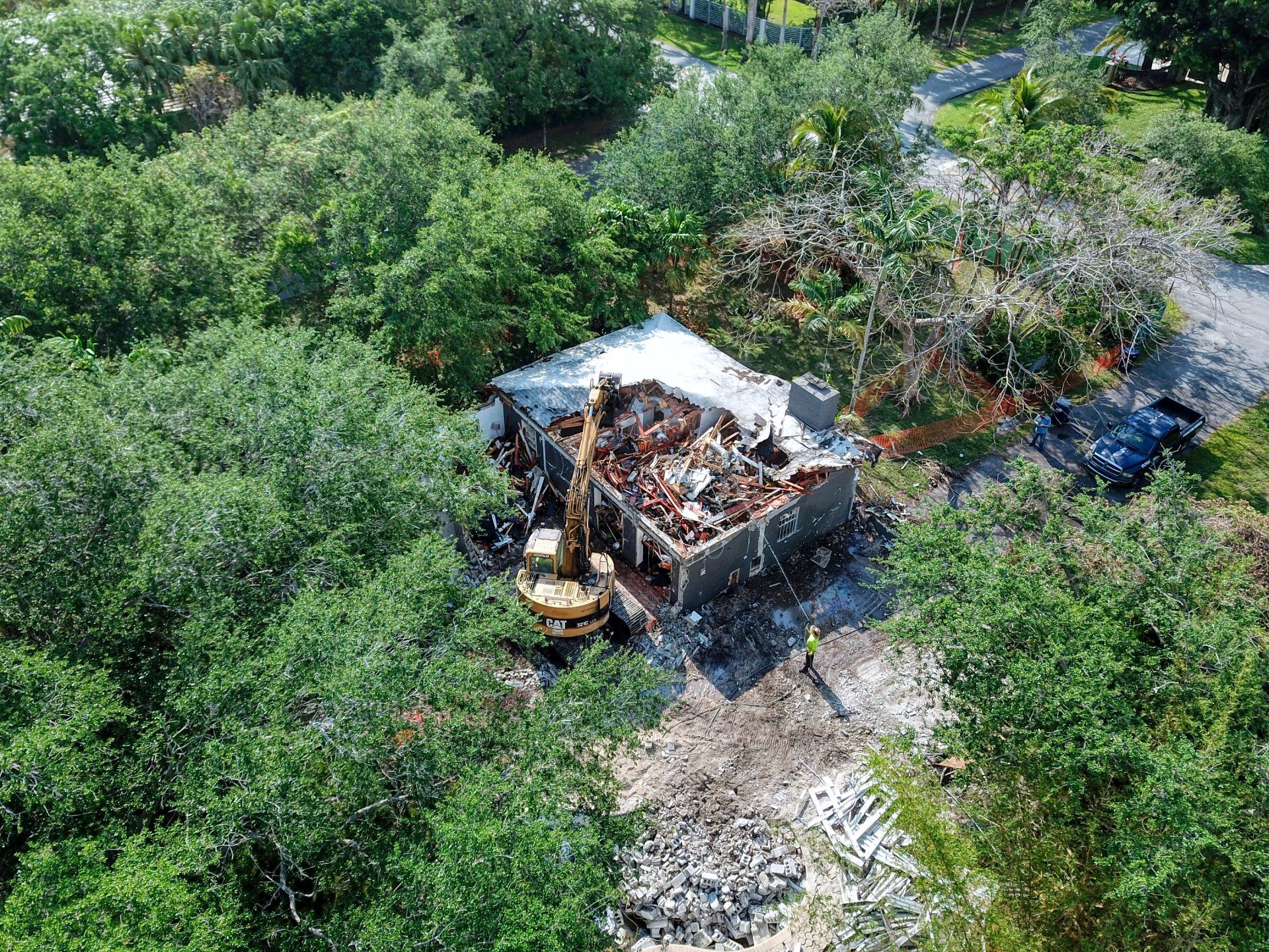 Demolition of a house, yellow excavator among trees, debris scattered.