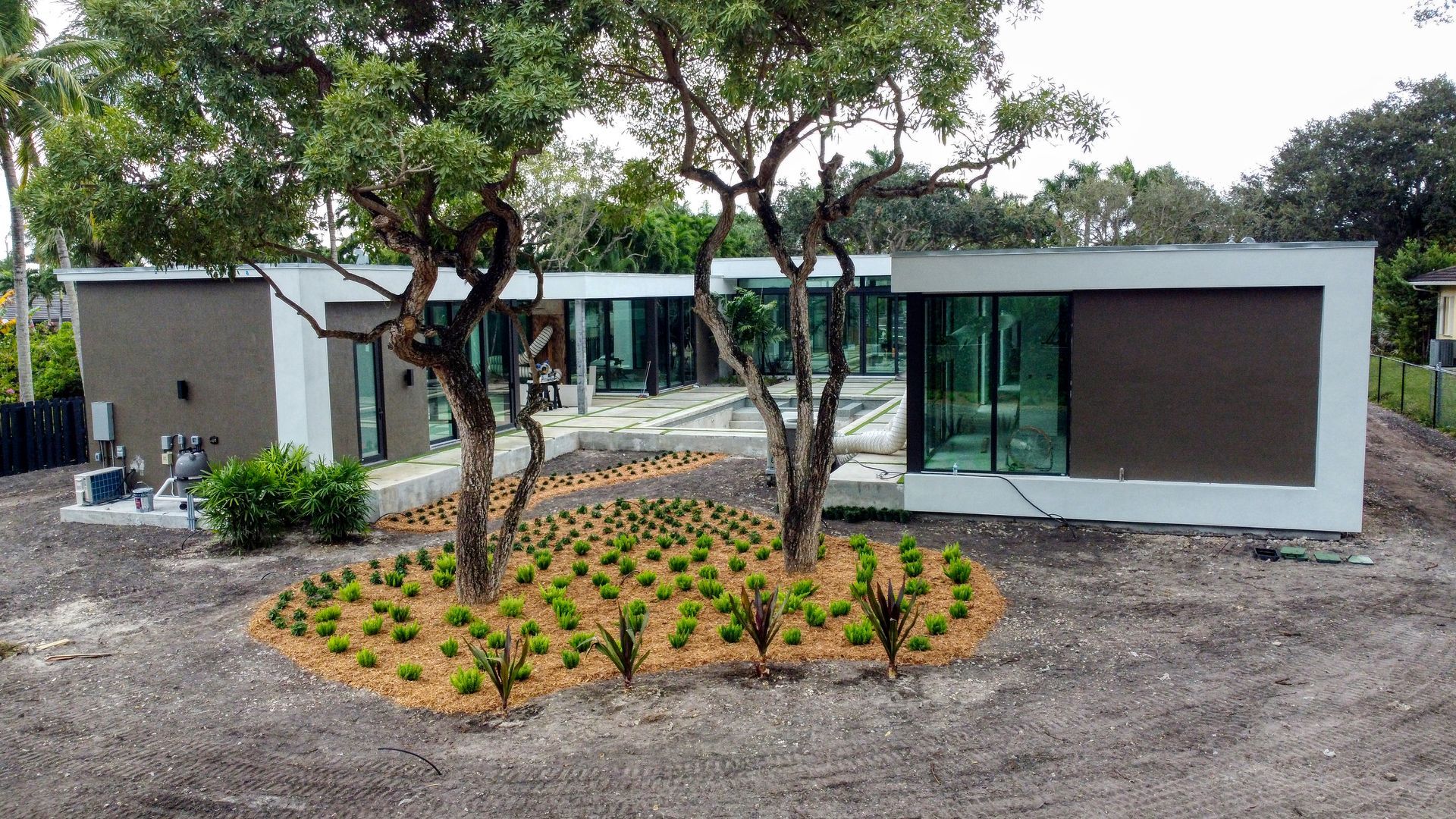 Modern house with large windows, brown and white exterior, two trees and landscaping.