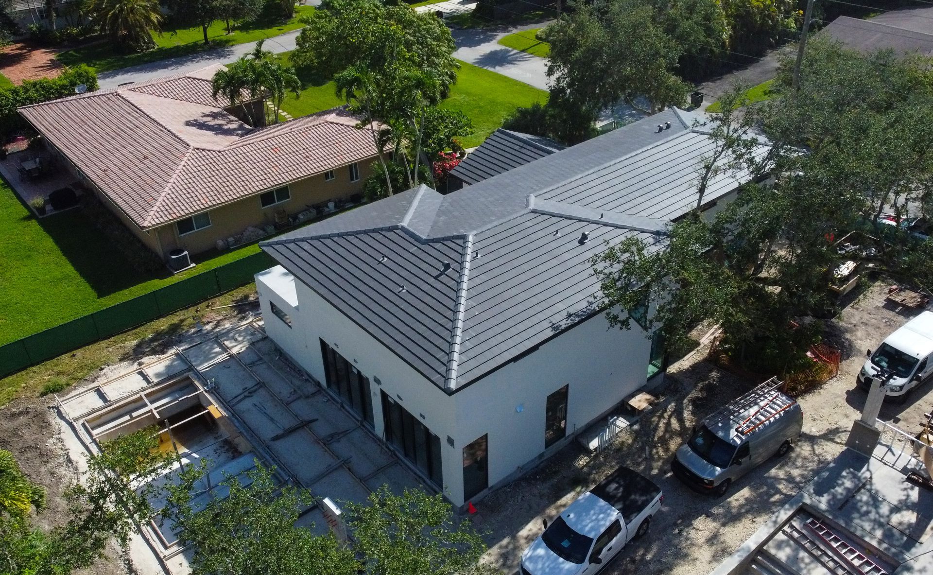 An aerial view of a newly constructed white house with a black roof and parked vehicles.