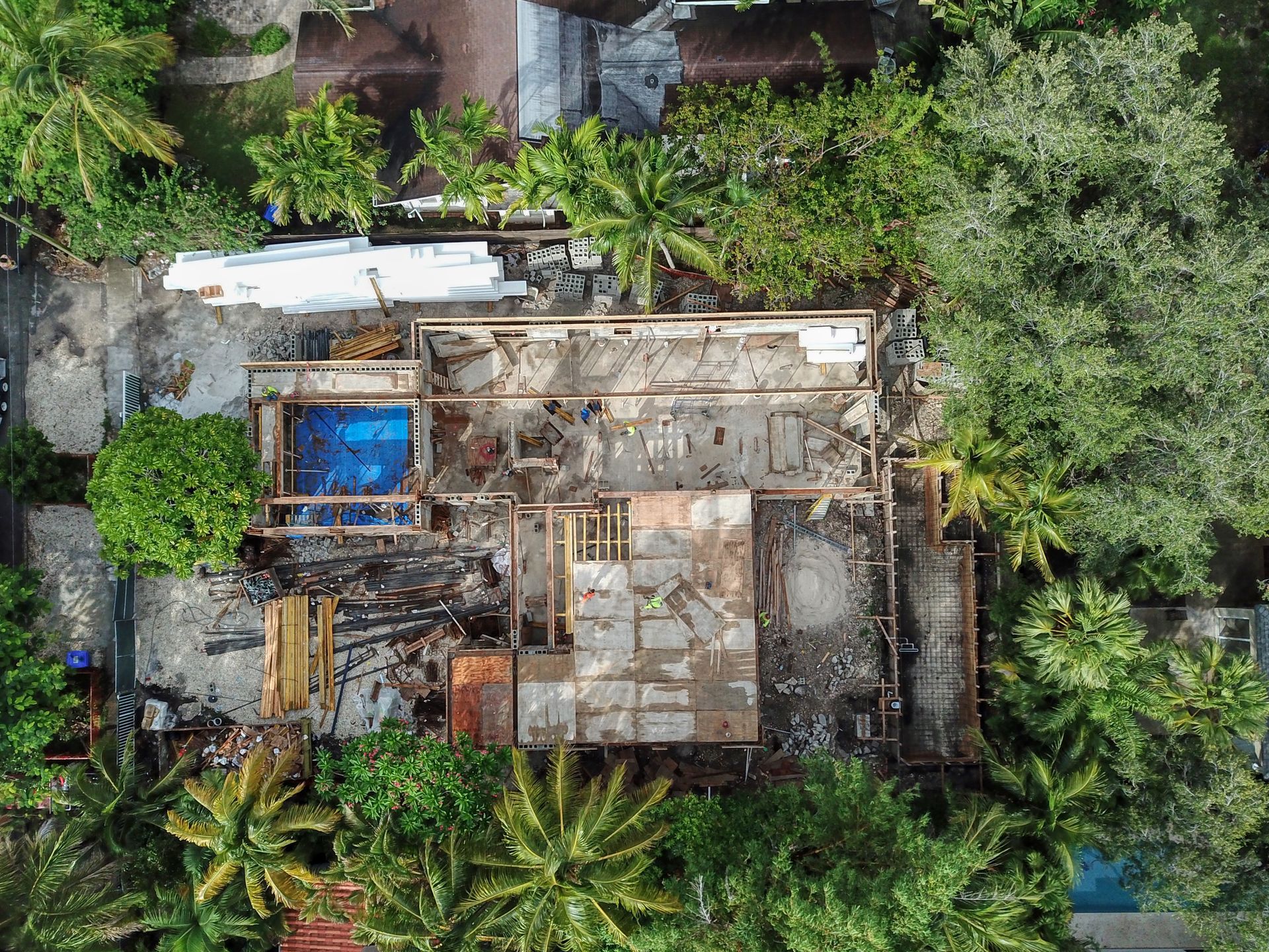 Aerial view of a building under construction, showing a partially demolished structure surrounded by trees and construction materials.