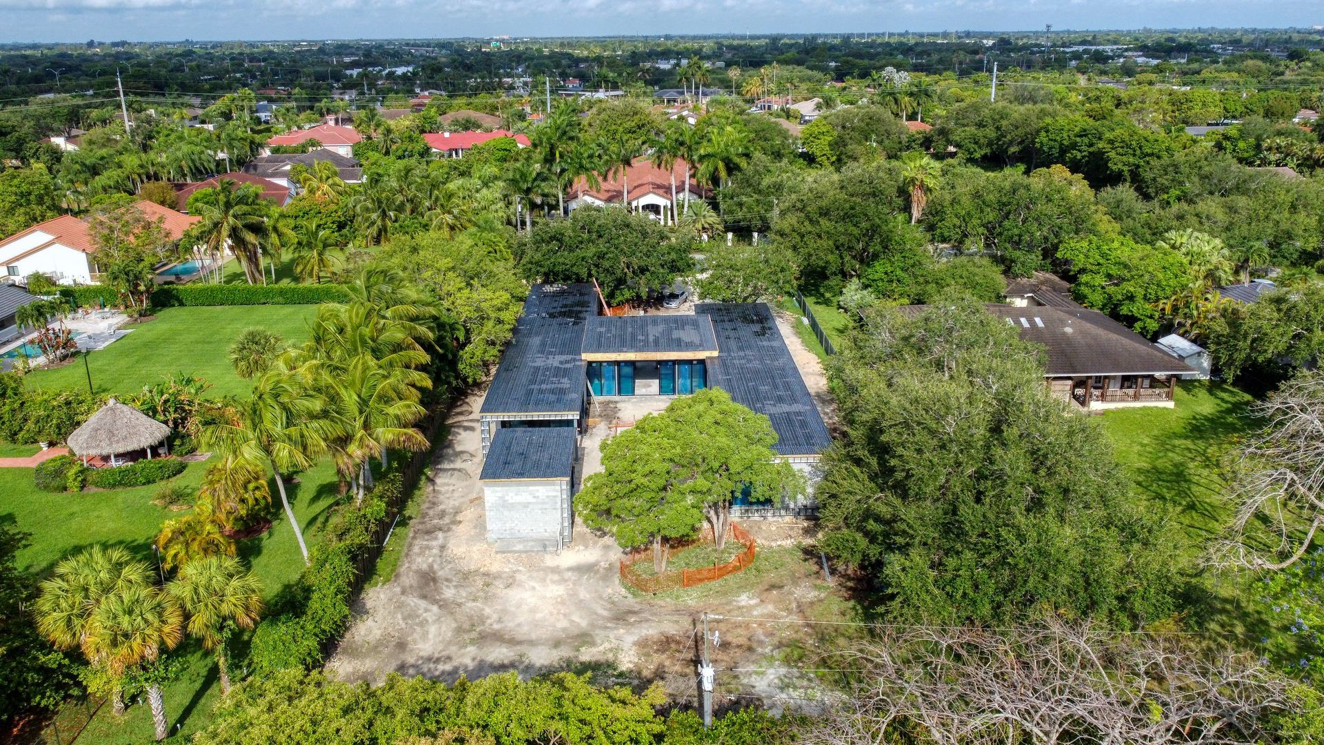Aerial view of a home with a blue roof, surrounded by trees and other houses in a suburban setting.