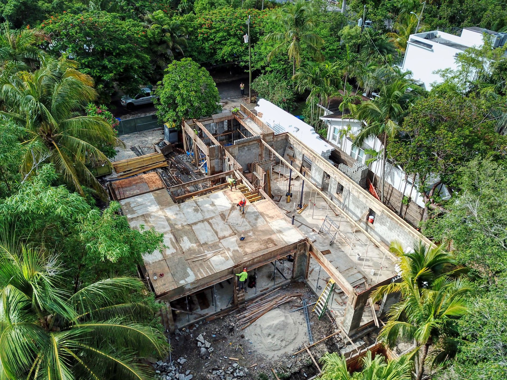 Aerial view of a building under construction, surrounded by lush green trees and foliage.