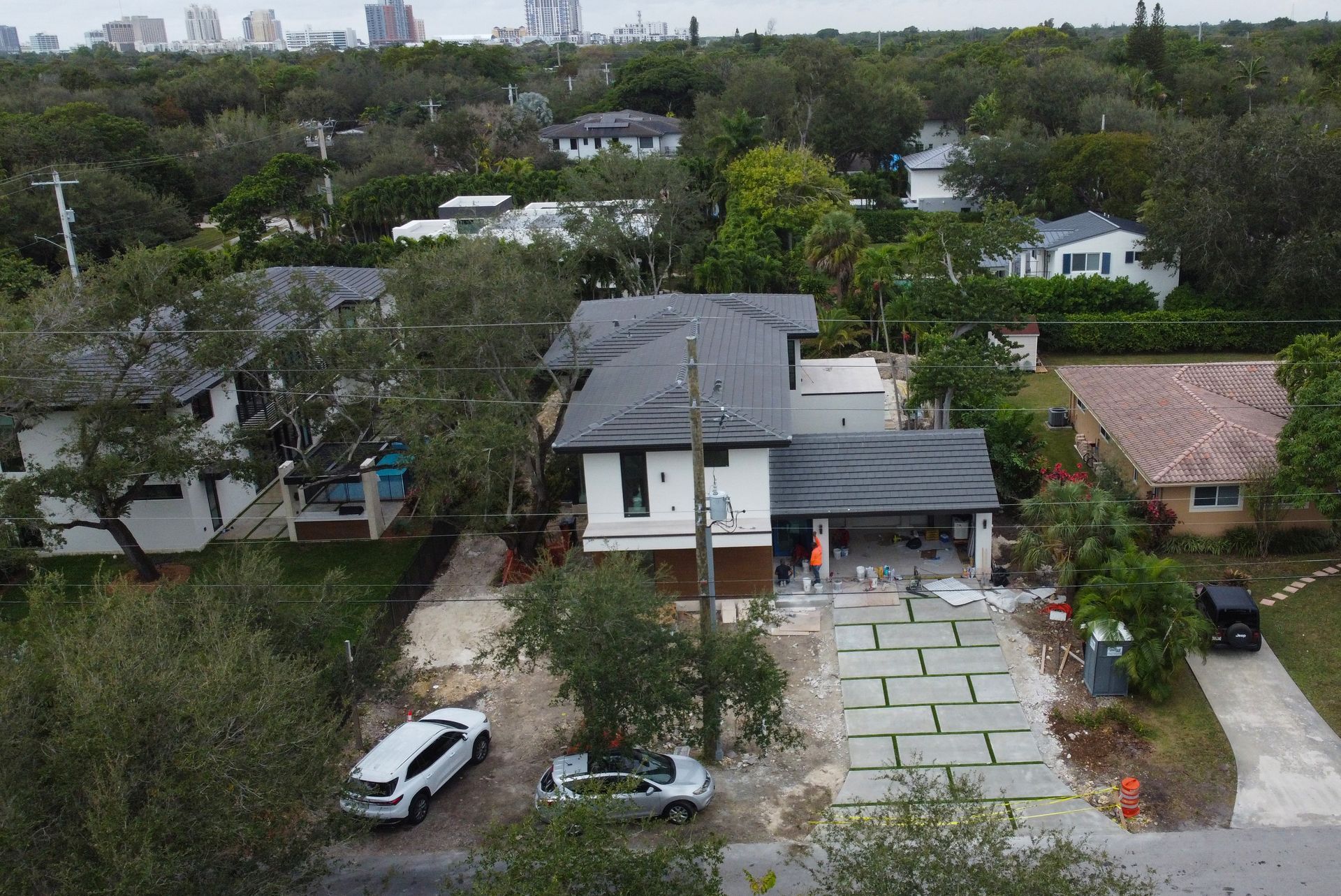 An aerial view of houses in a residential neighborhood, with trees, driveways, and construction materials visible.