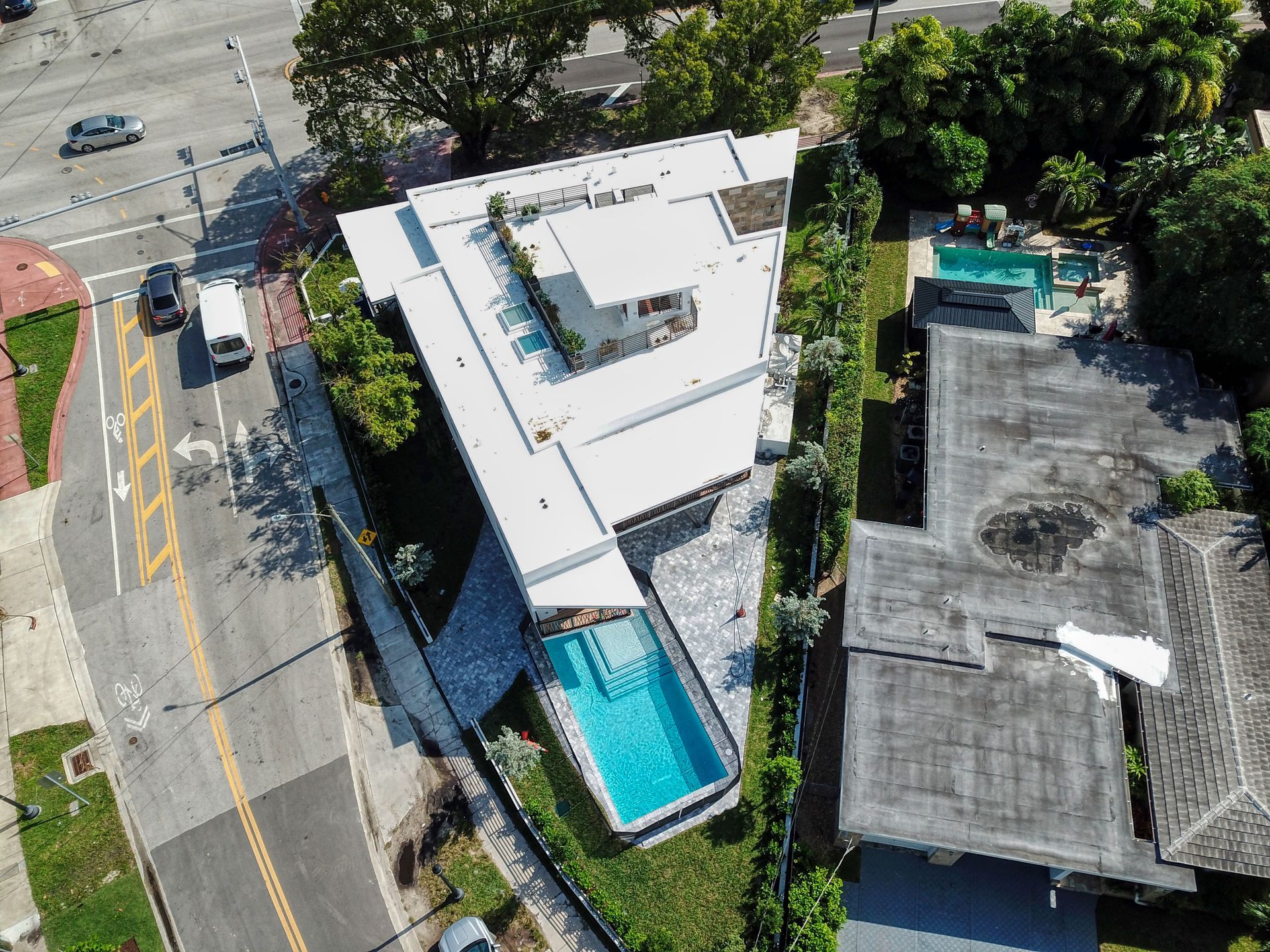 Aerial view of modern white house with a pool, next to a street with cars.