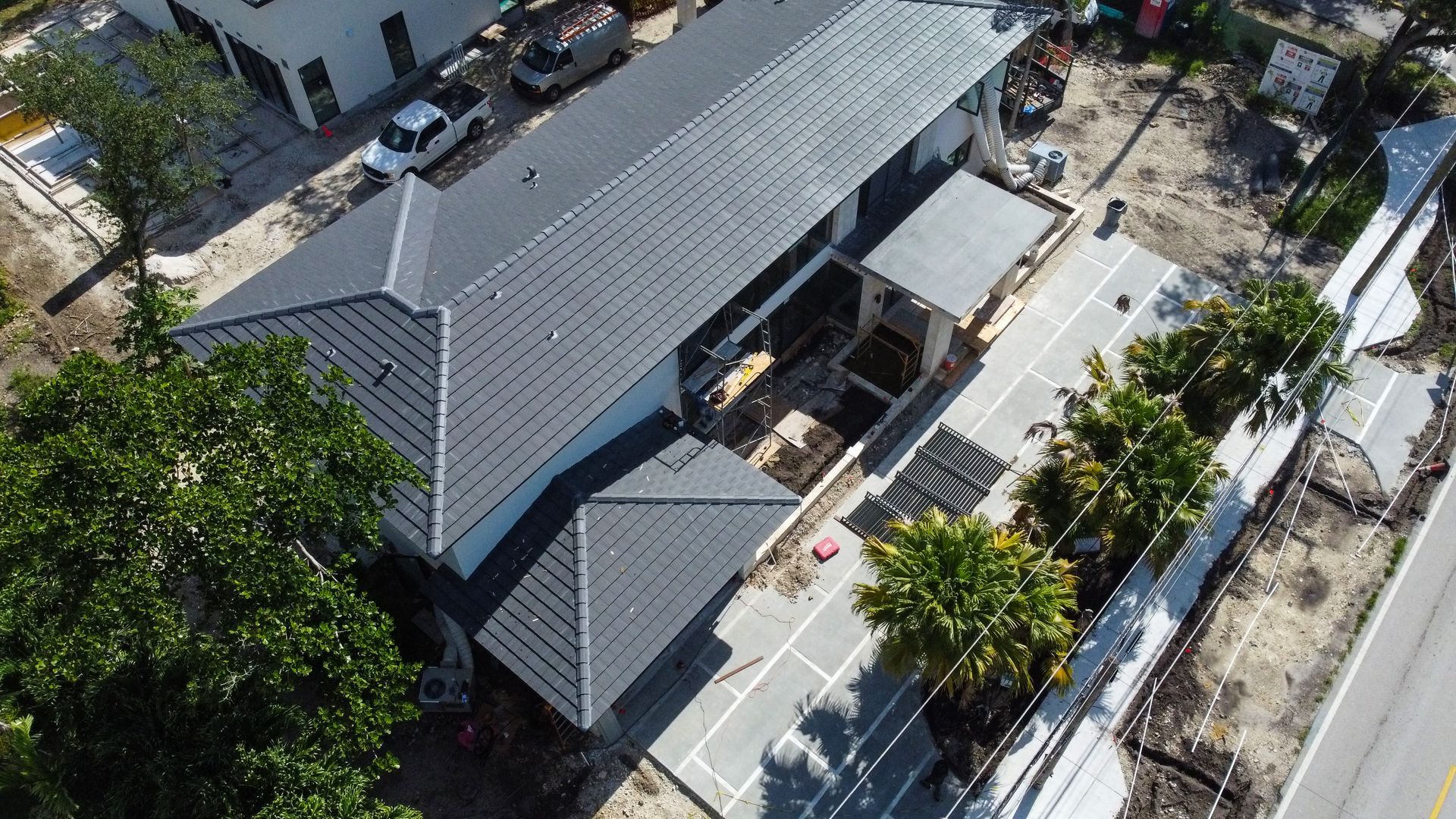 Aerial view of a building with a dark gray roof, parking spaces, and some greenery along a street.