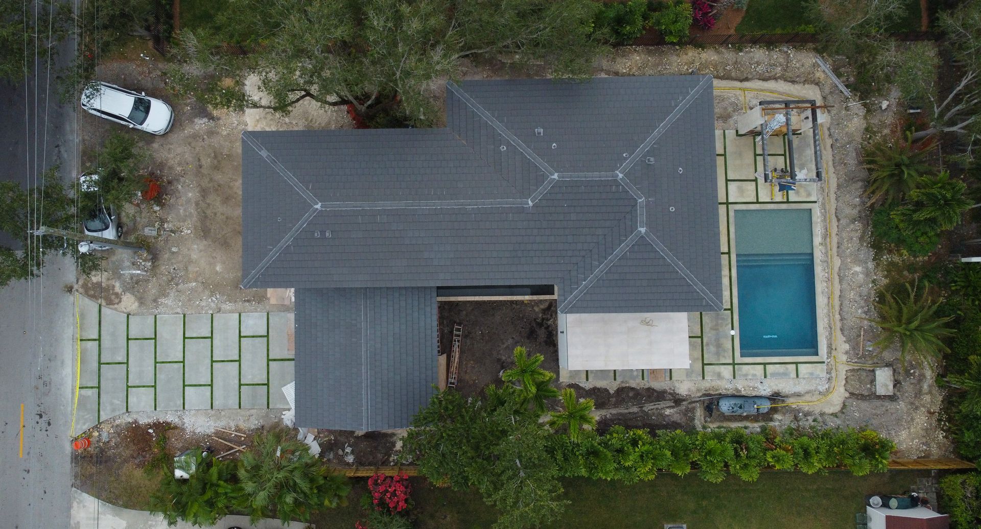 Aerial view of a house with a dark gray roof, swimming pool, and stone driveway.