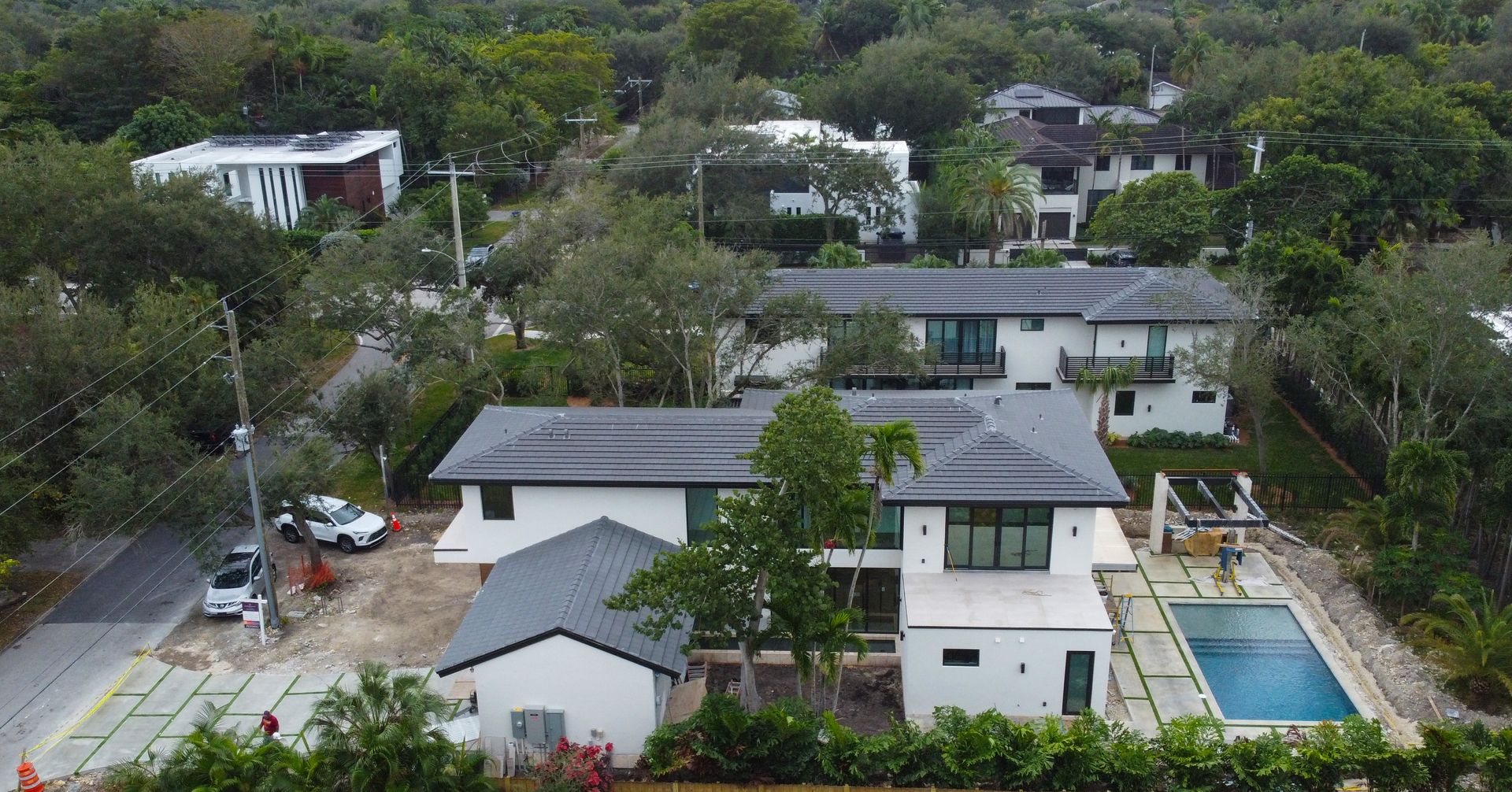 Aerial view of modern white house with a pool, trees, and other buildings nearby.