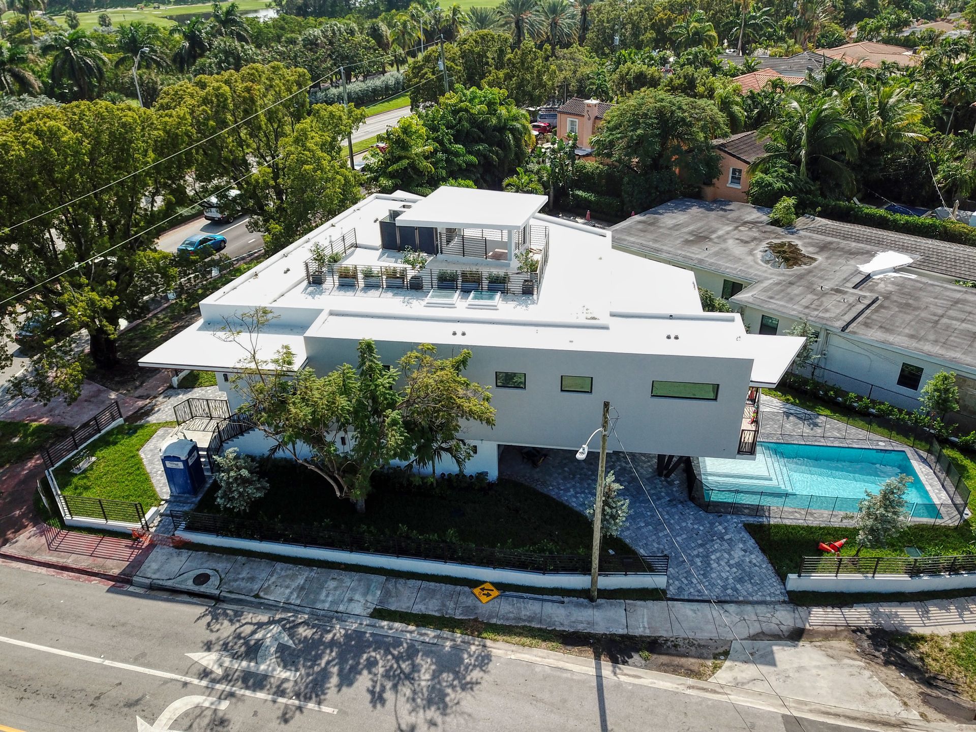 Modern white house with a rooftop patio, swimming pool, and lush landscaping.