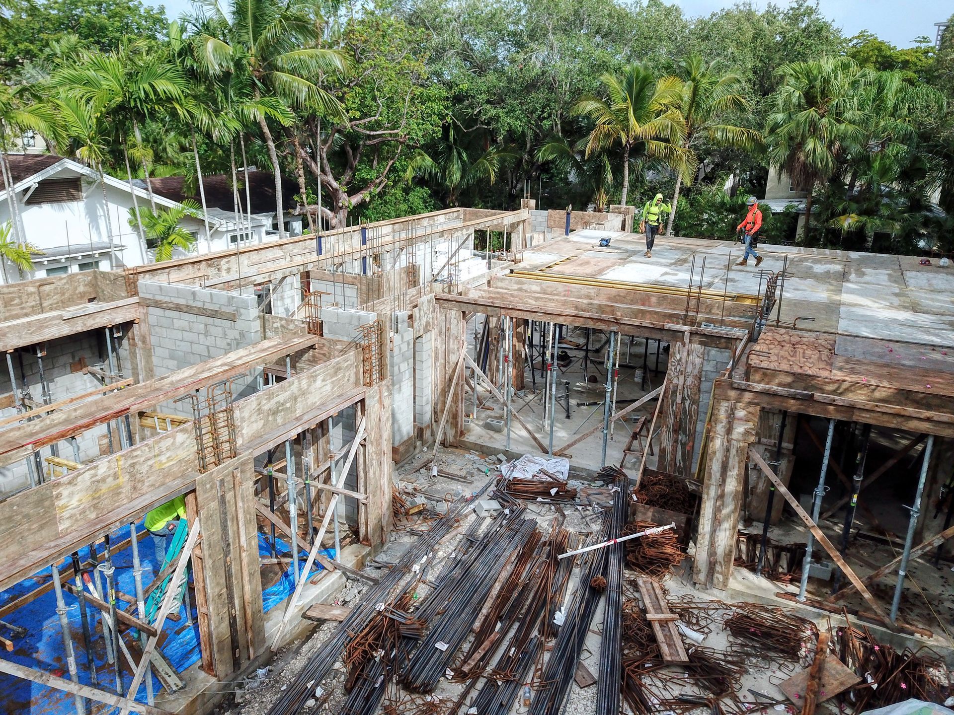 Construction site: concrete framework, exposed rebar, scaffolding, and workers. Trees in the background.
