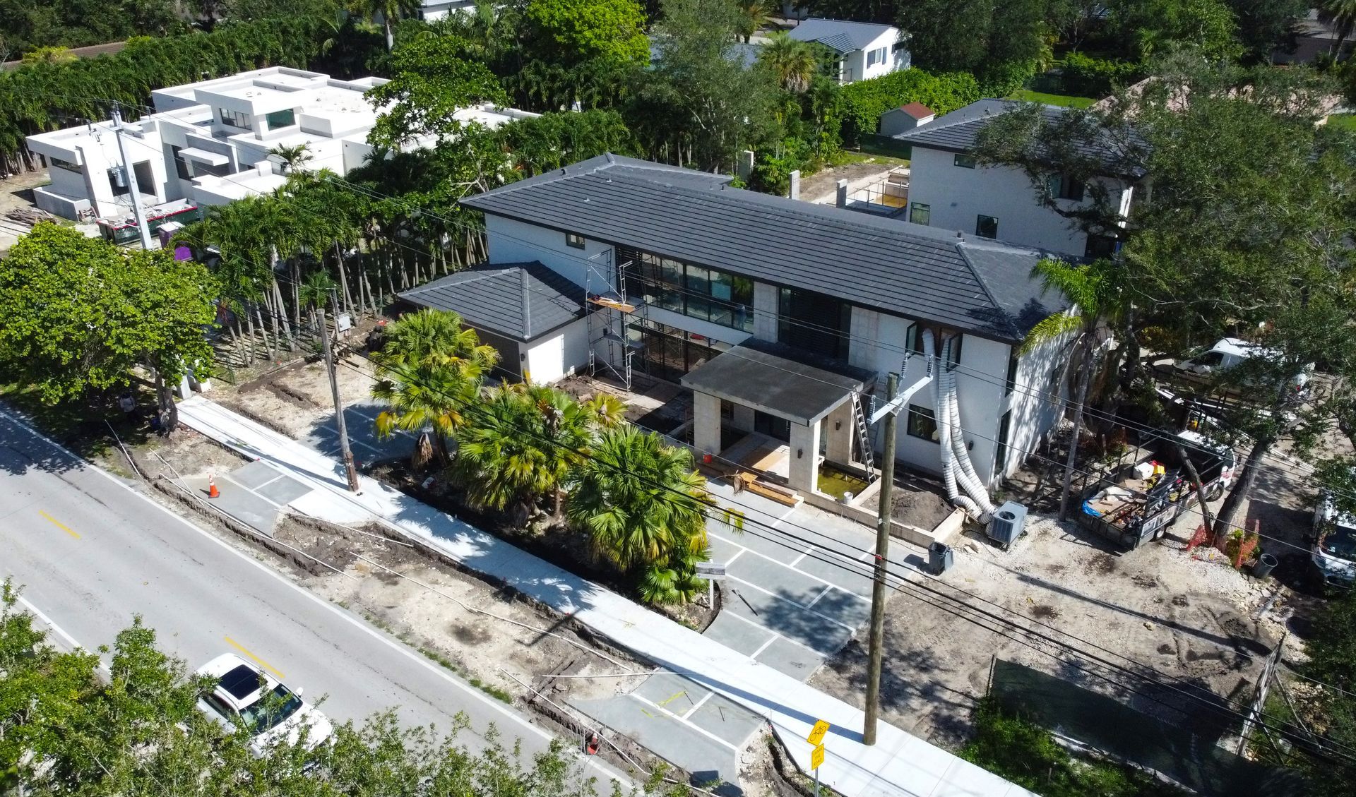 Aerial view of a two-story white house with a black roof next to a road, trees, and construction.