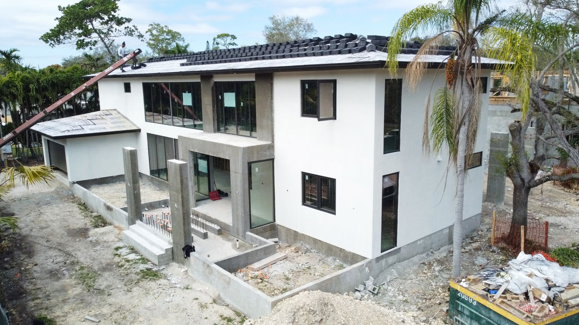 Two-story house under construction with white stucco, black window frames, and concrete accents.