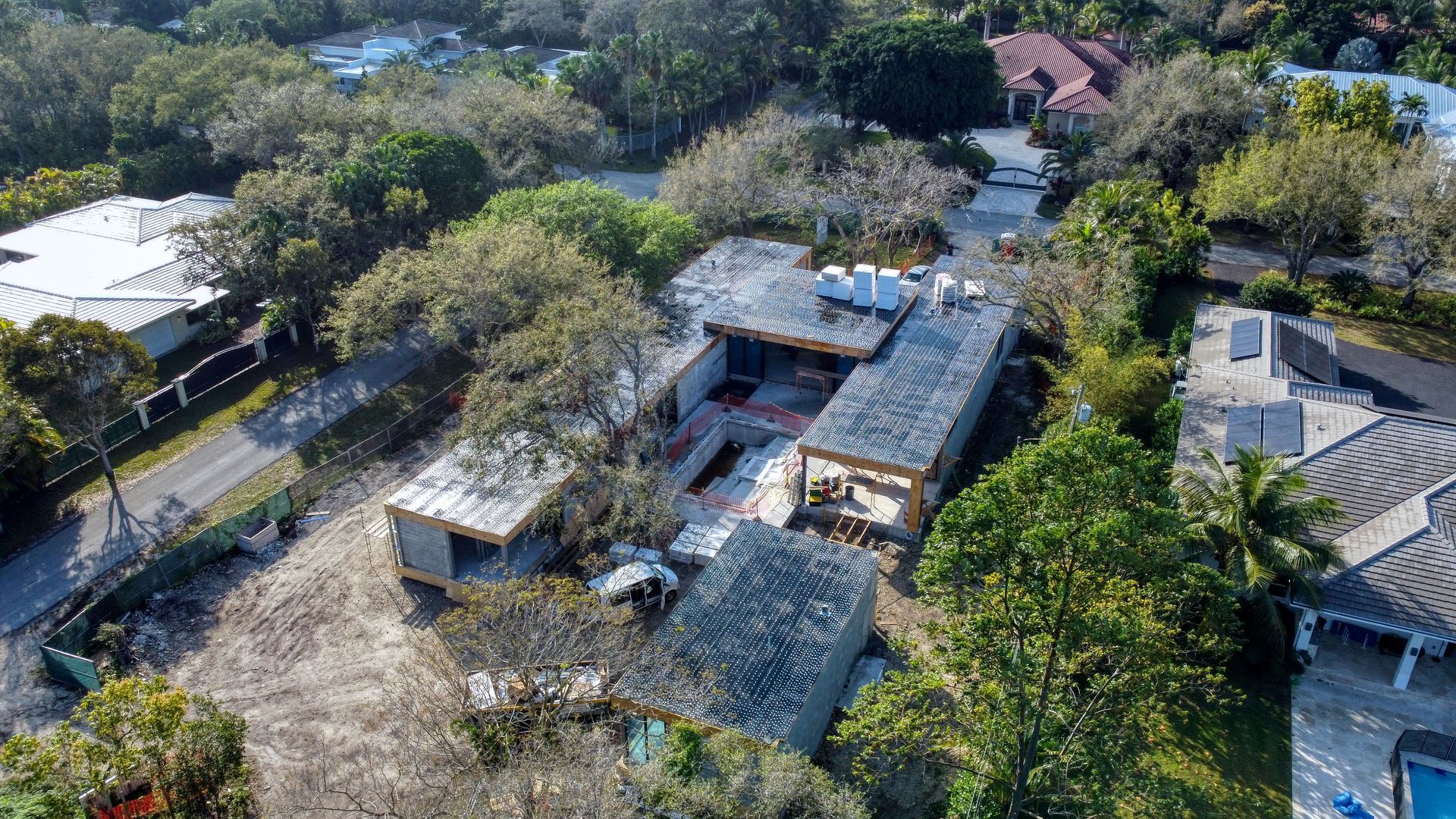 Aerial view of a home under construction surrounded by trees and other houses.