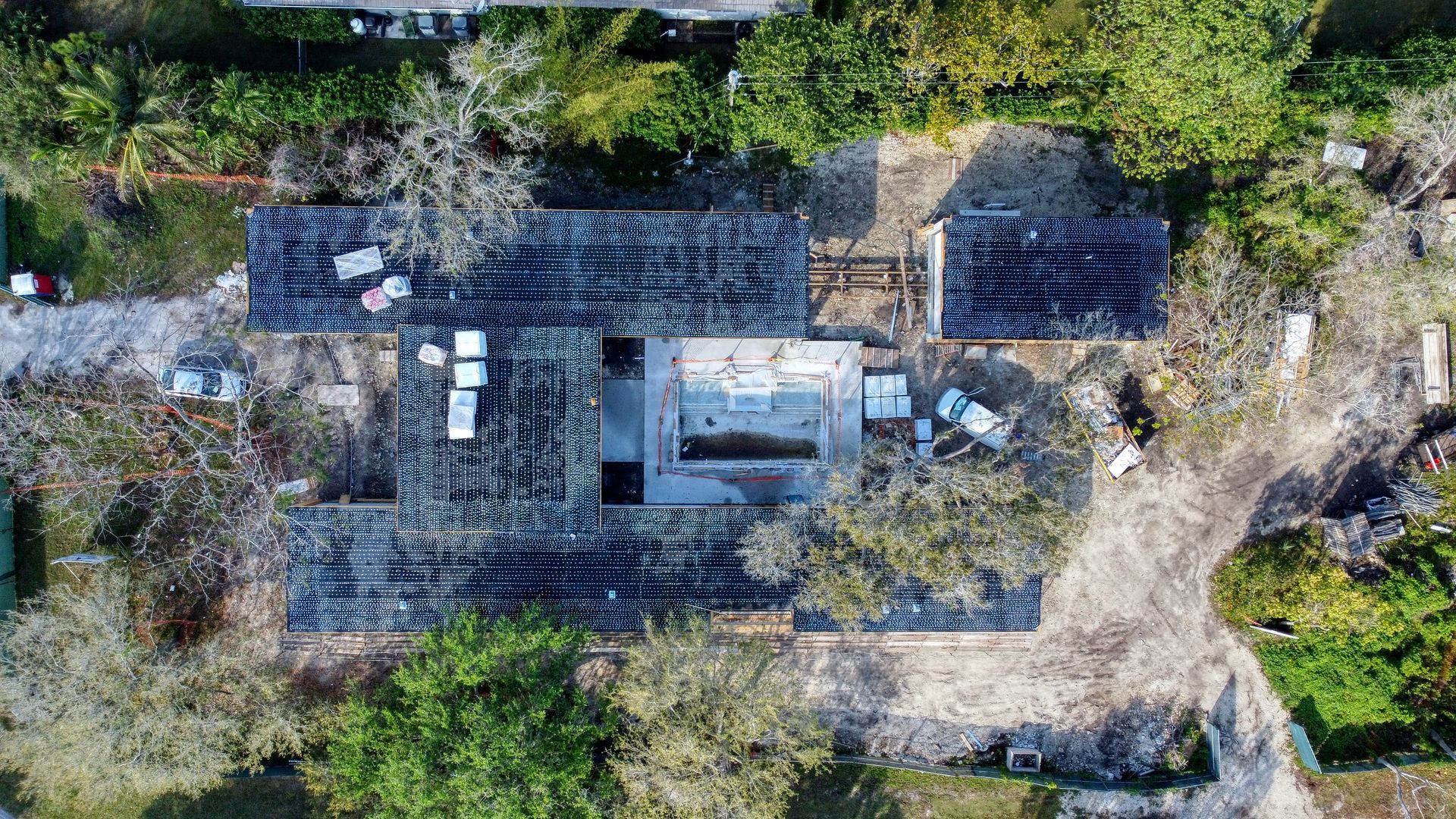 Overhead view of a building's roof with large sections missing. Surroundings include trees and dirt paths.