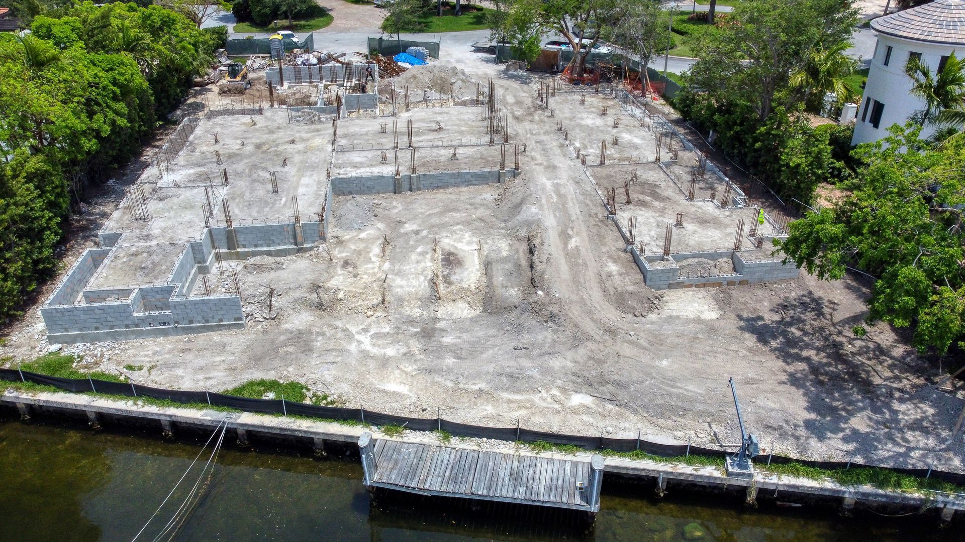 Construction site with concrete foundation and pilings, next to a waterway.