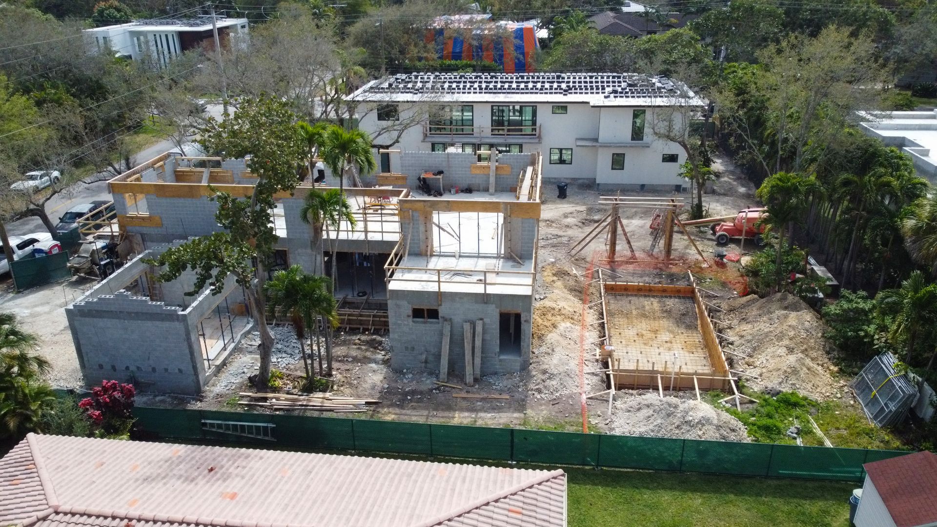 Construction site with multiple concrete structures in progress, surrounded by trees and green fencing.