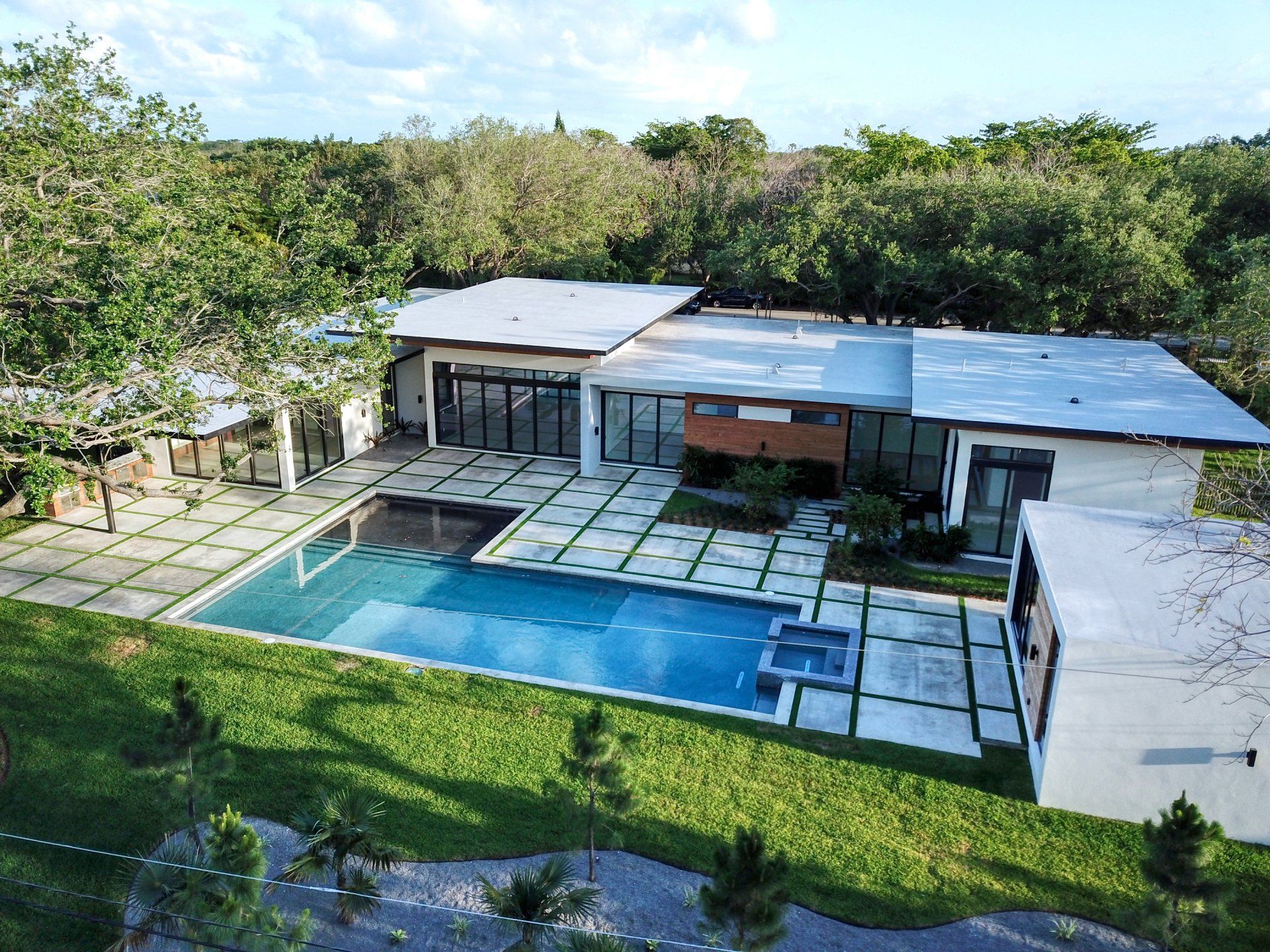 Modern home with pool and patio surrounded by green grass and trees.