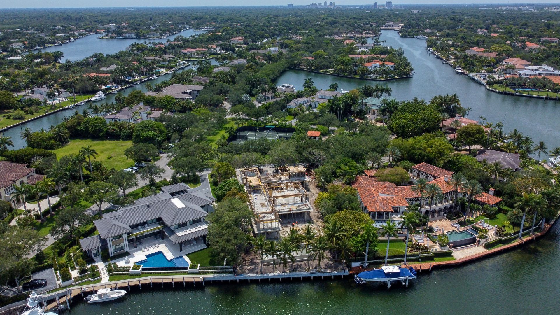 Aerial view of waterfront houses with boats and canals; lush green trees and foliage.