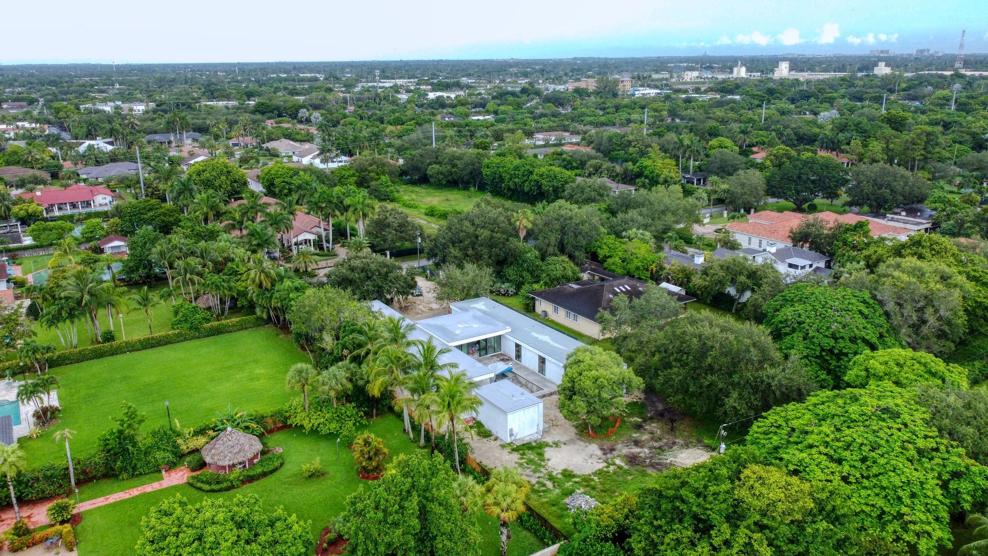 Aerial view of a suburban neighborhood with houses, green lawns, and dense trees under a cloudy sky.