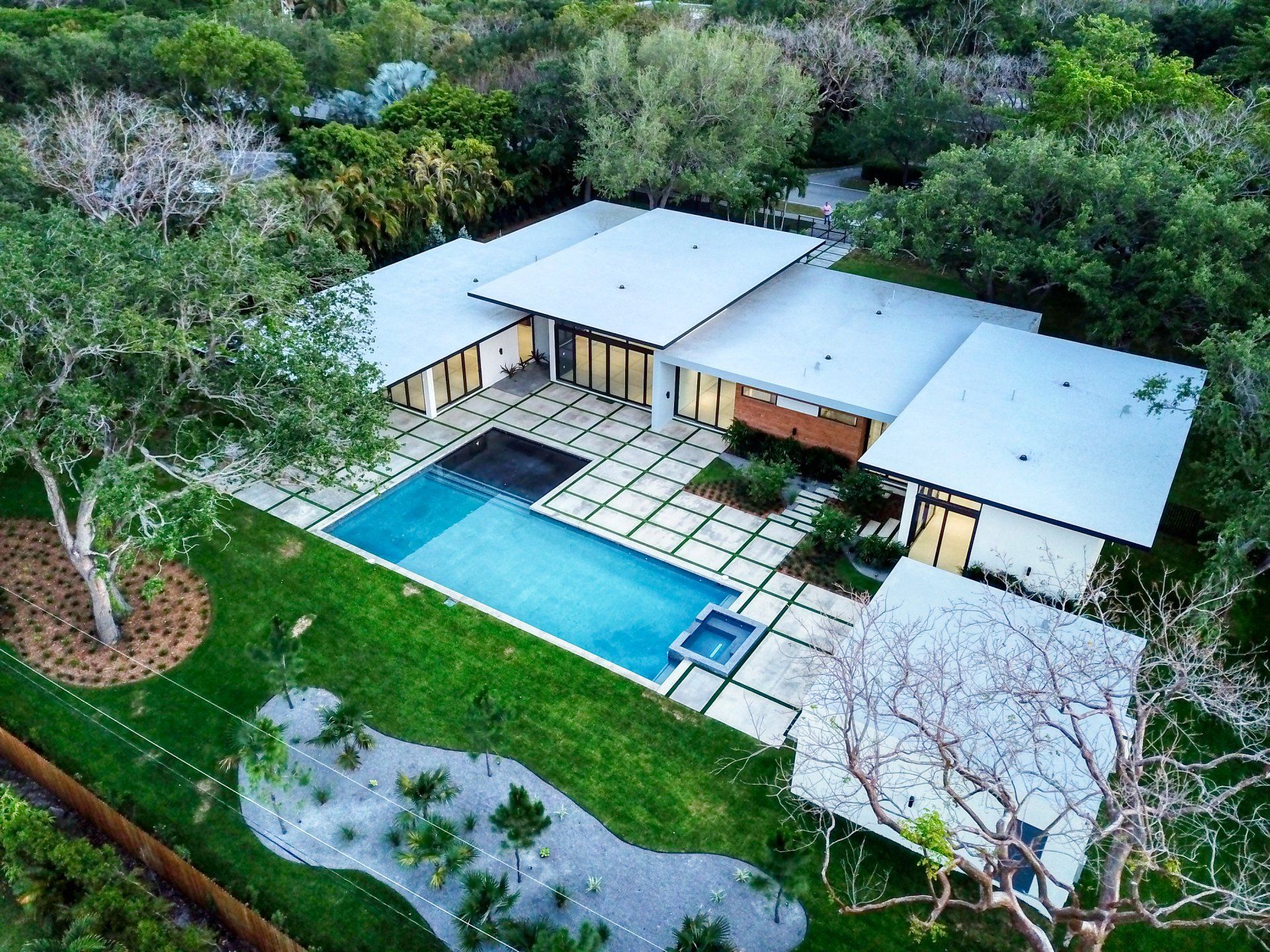 Modern home with pool and patio, surrounded by lush green landscaping and trees.
