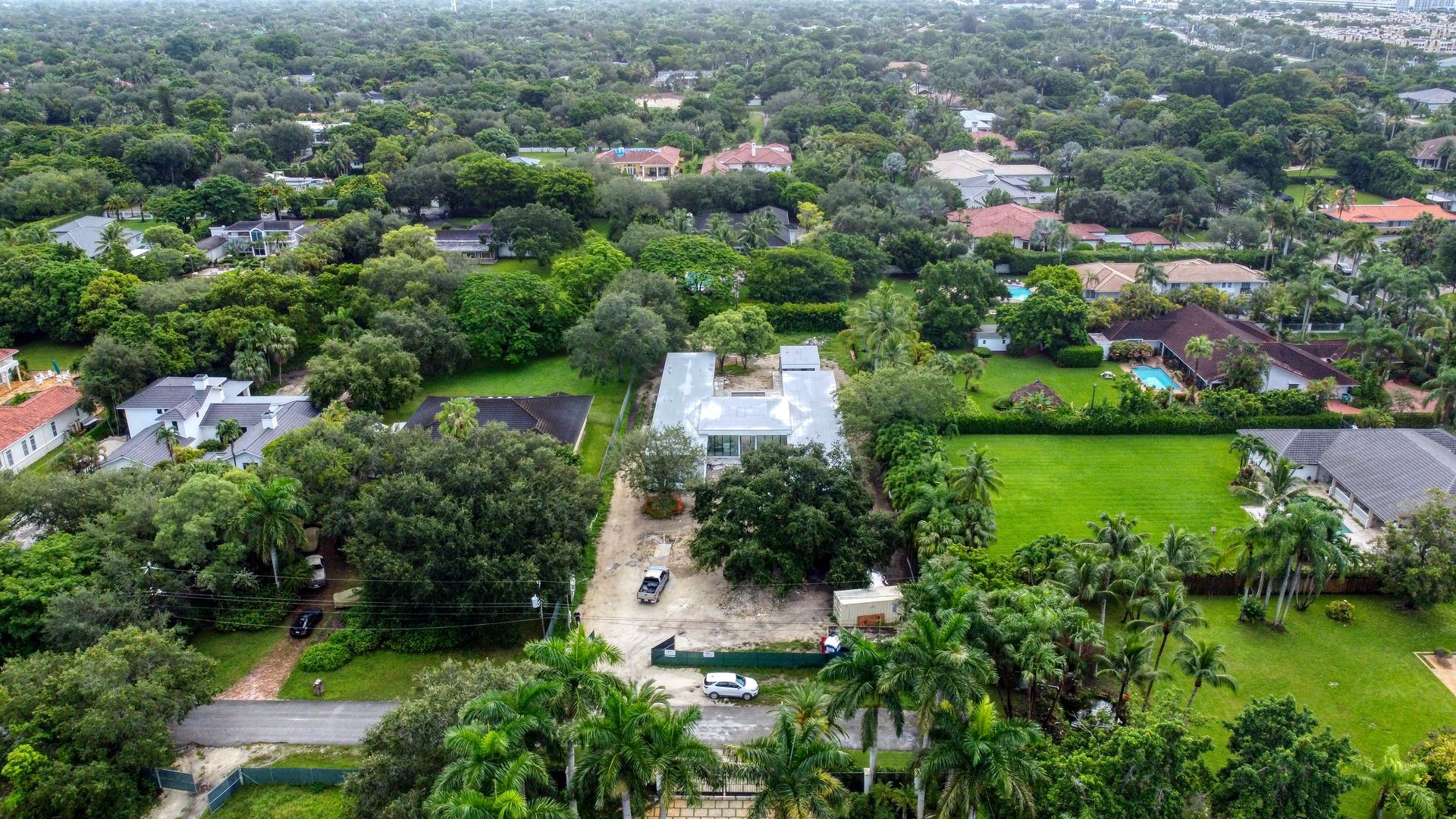 Aerial view of a suburban neighborhood with large houses, green lawns, and dense tree cover.