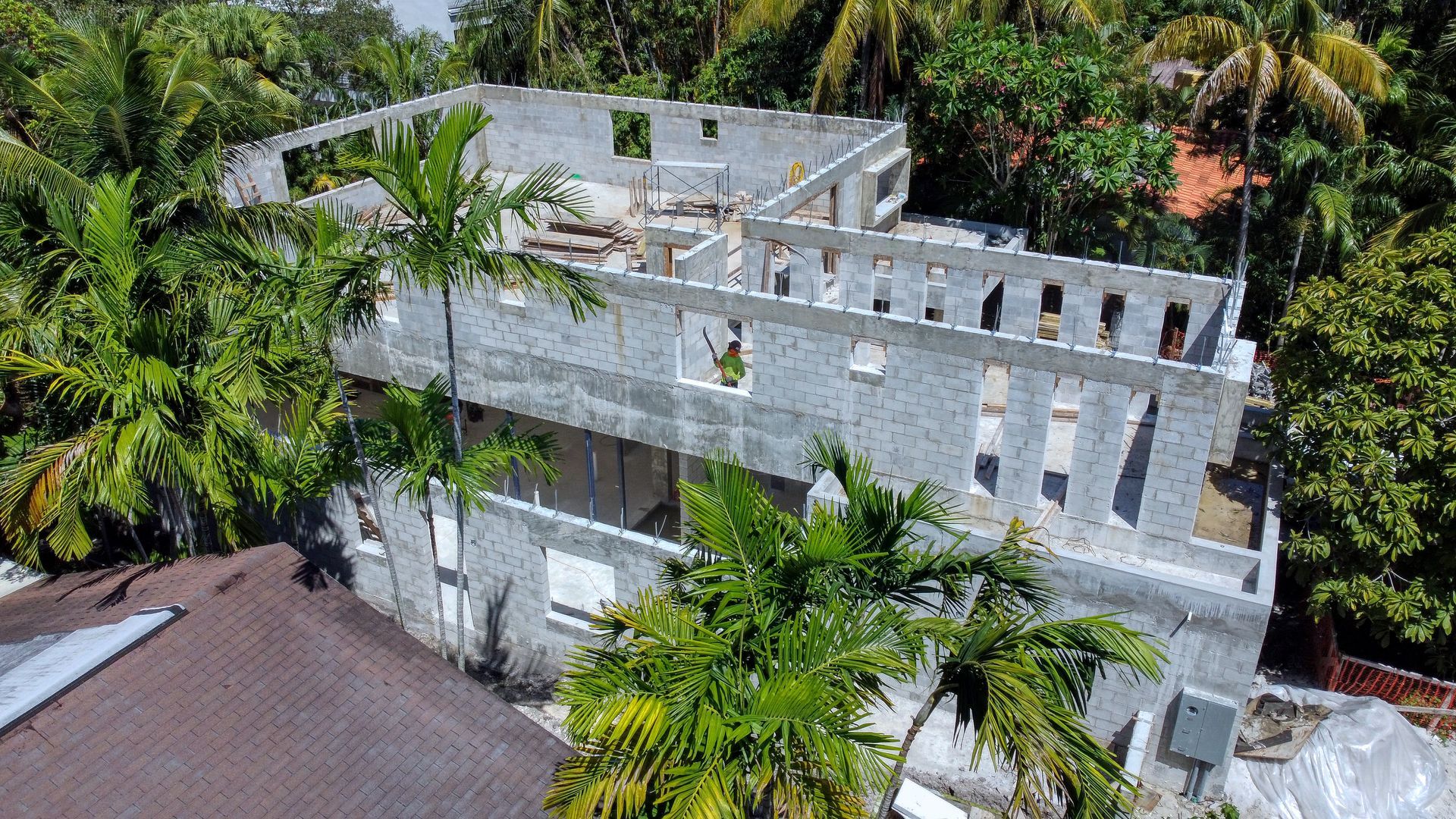 Unfinished concrete building under construction, surrounded by lush green trees, daytime.