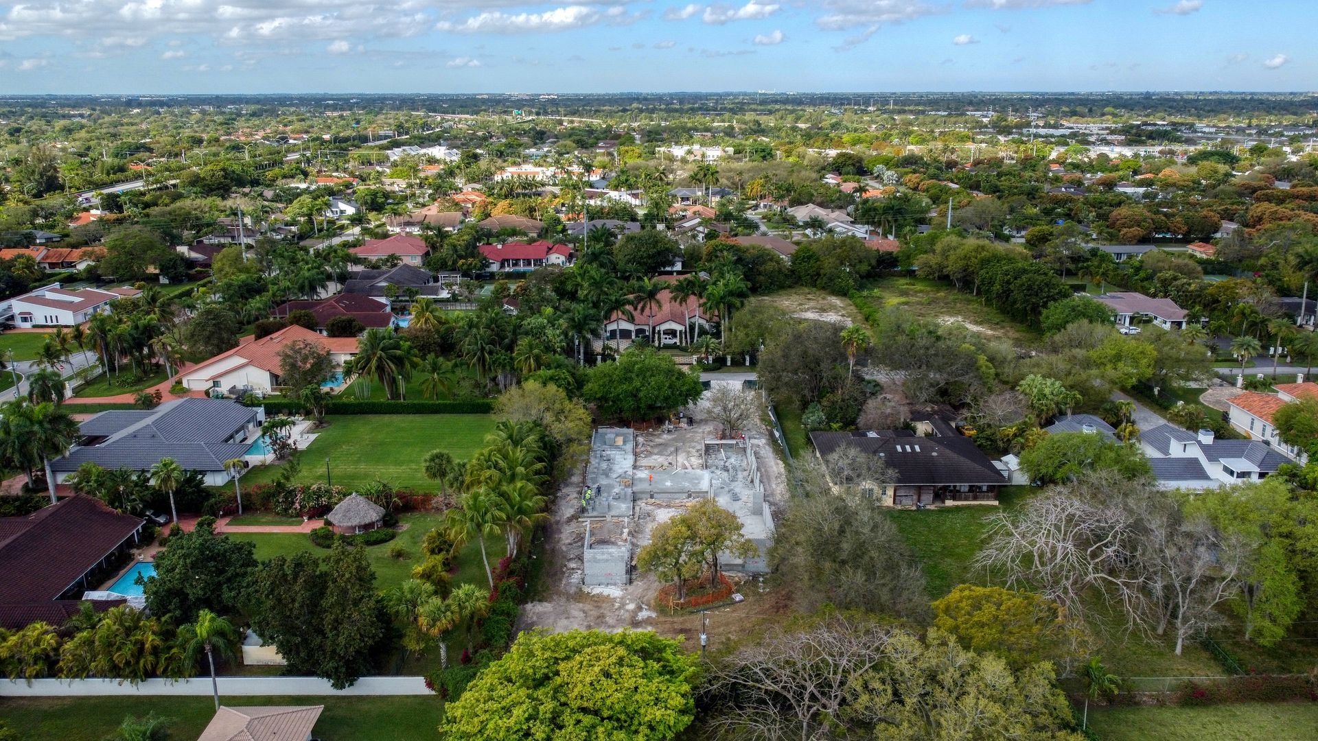 Aerial view of a residential area with houses surrounded by lush green trees and a construction site.