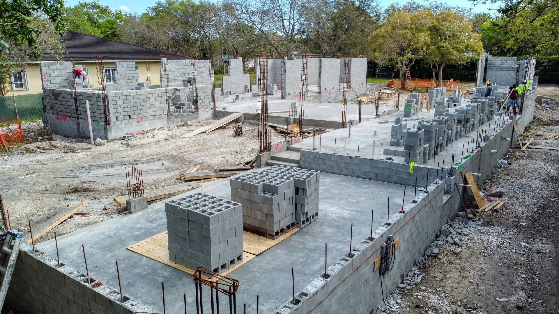 Construction site with concrete block foundation and partially built walls; workers are present.