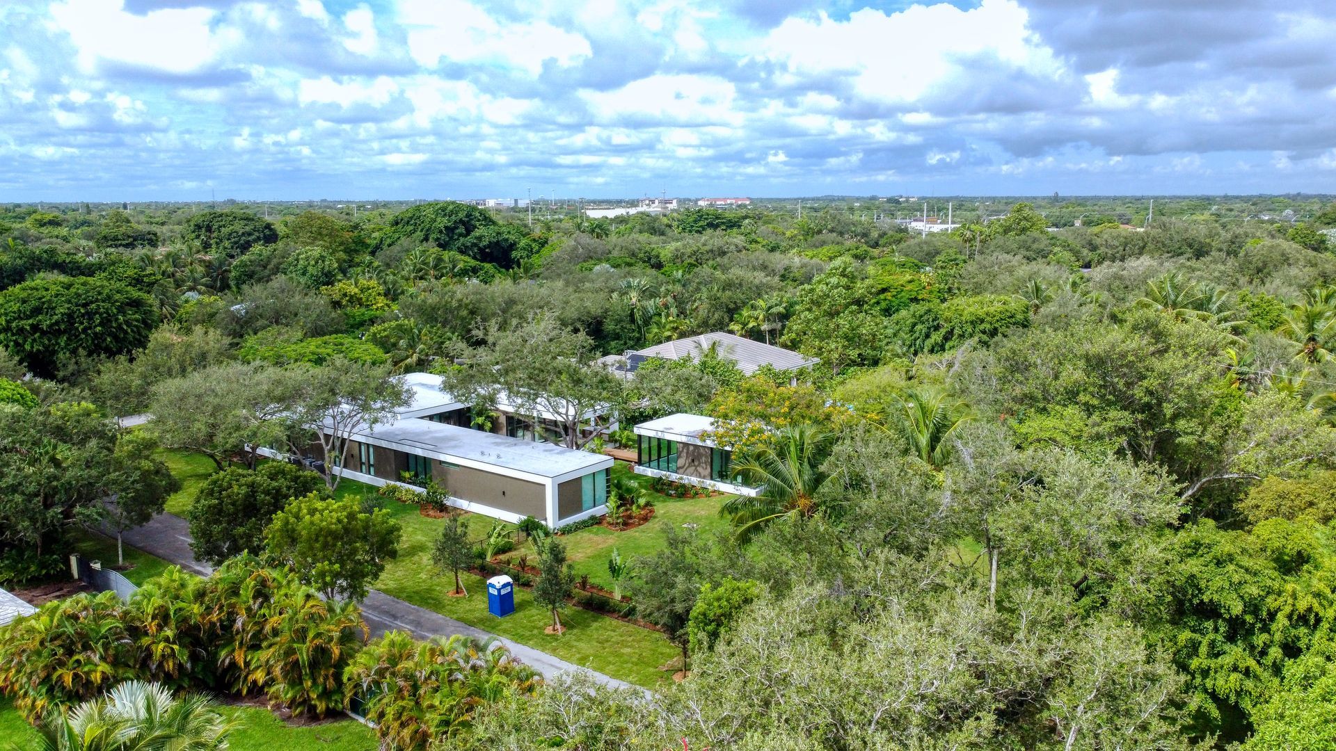 Aerial view of modern homes nestled amongst lush green trees under a cloudy sky.