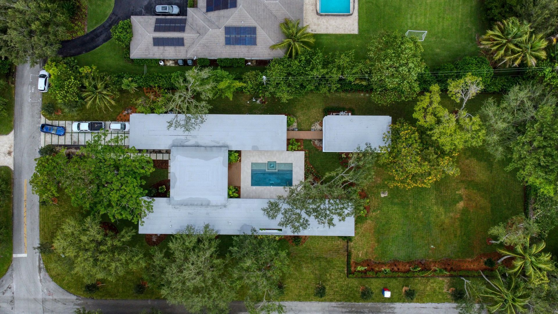 Aerial view of a mid-century modern home with a pool, surrounded by green lawns and trees.