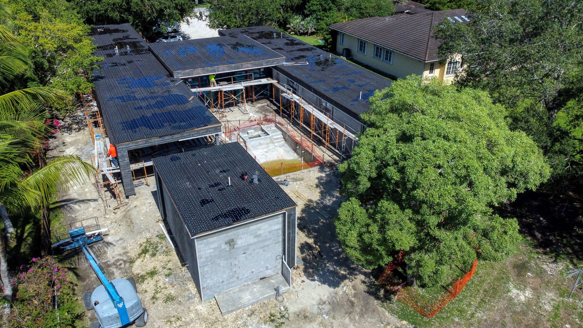 Overhead view of a modern house under construction, surrounded by trees and a construction area.